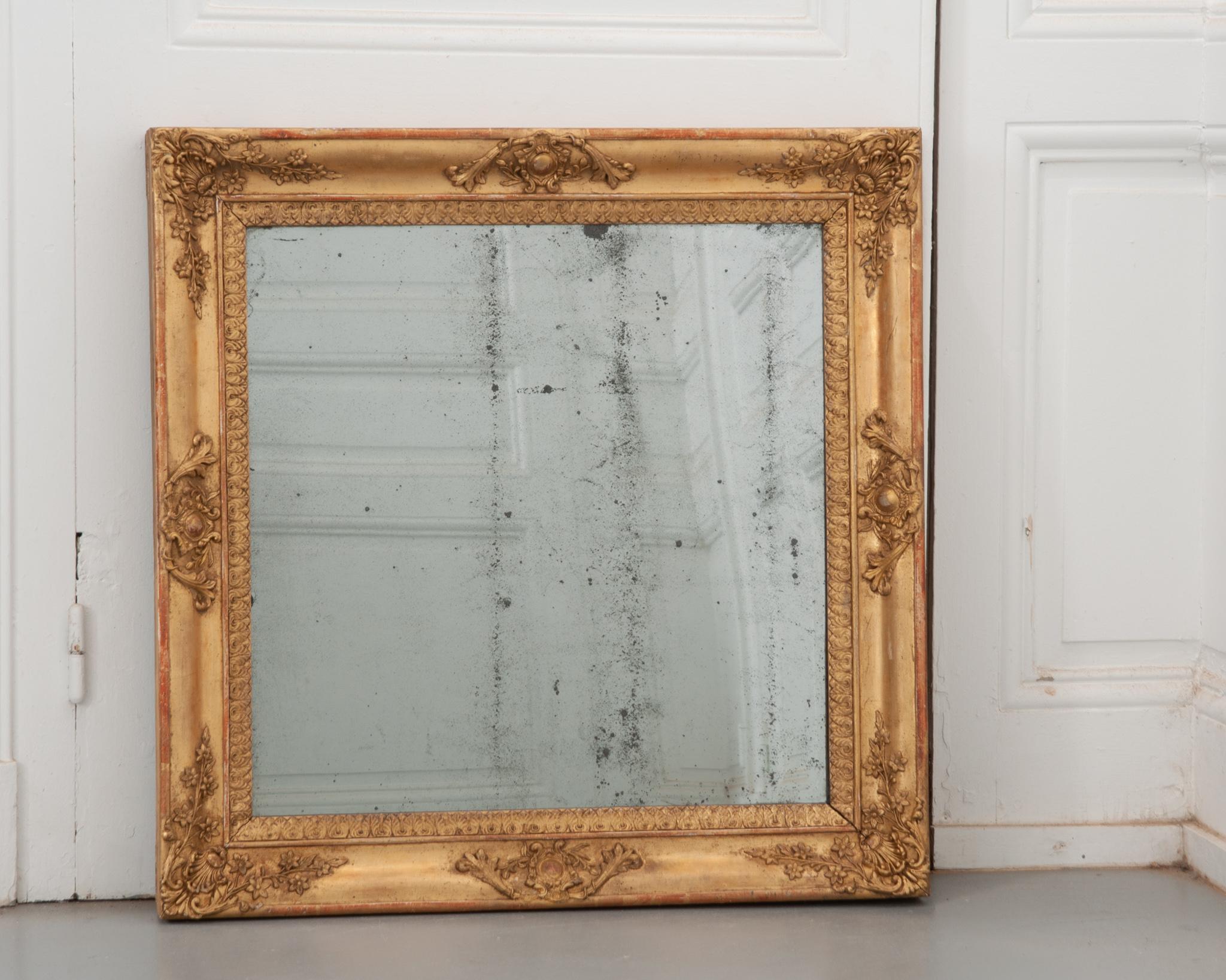 A stunning, symmetrical Empire style mirror from 19th century France! With its original mirror plate, some wonderful foxing is present while providing a clear reflection. The square frame is dripping with hand carved details on each side; crests