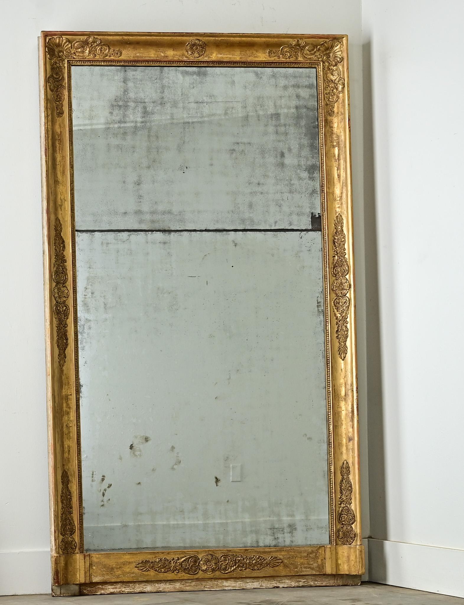 This French Empire mantle mirror (c. 1800) shows very careful surface decoration, the gold gilt molding is largely plain and smooth, with tight feather and foliate carvings placed at regular intervals along the perimeter. The original mirror plate