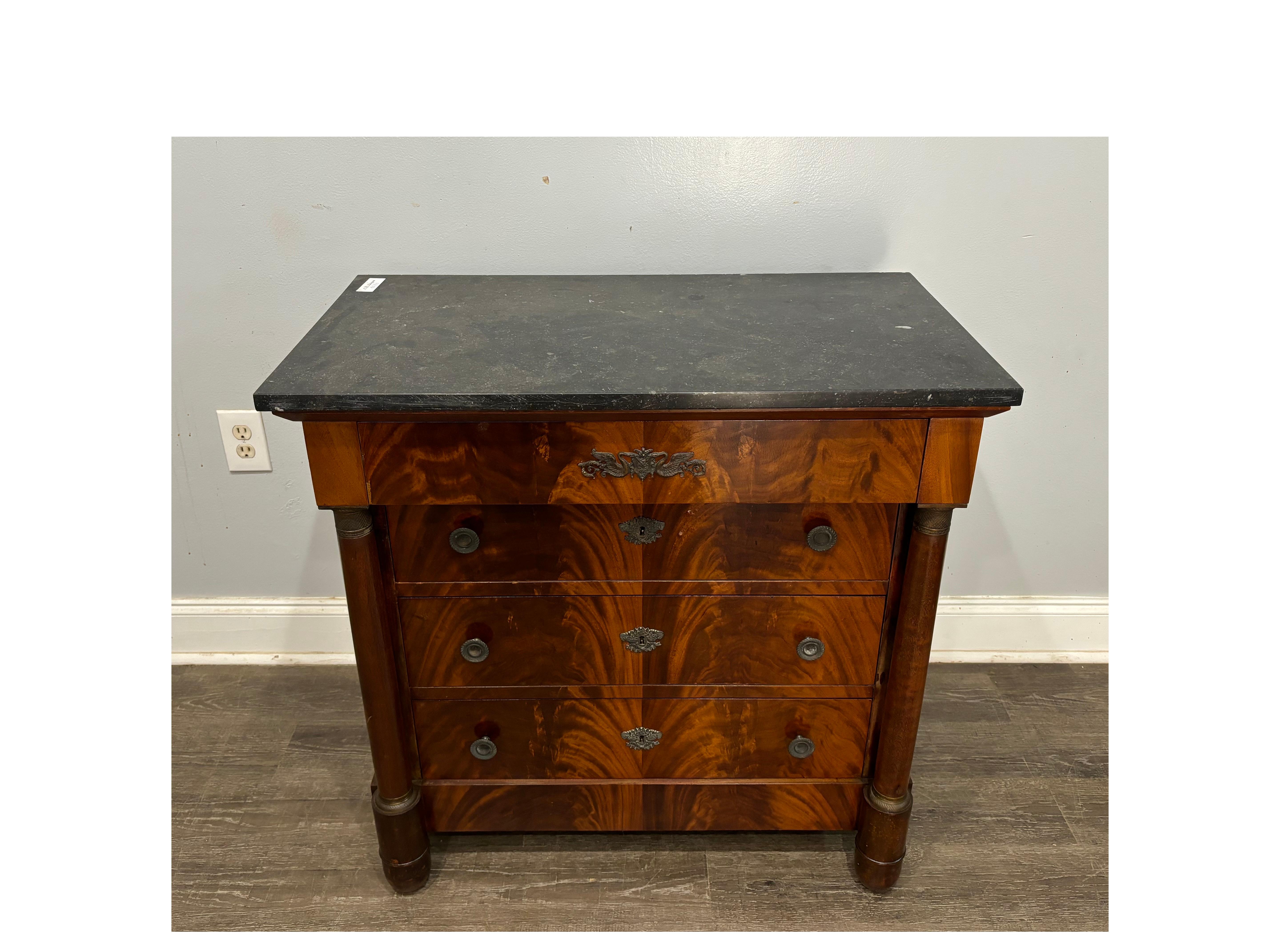This Charming Small Empire Commode is made of mahogany with a black marble top. It has bronze rings around the columns. Easy to place anywhere.