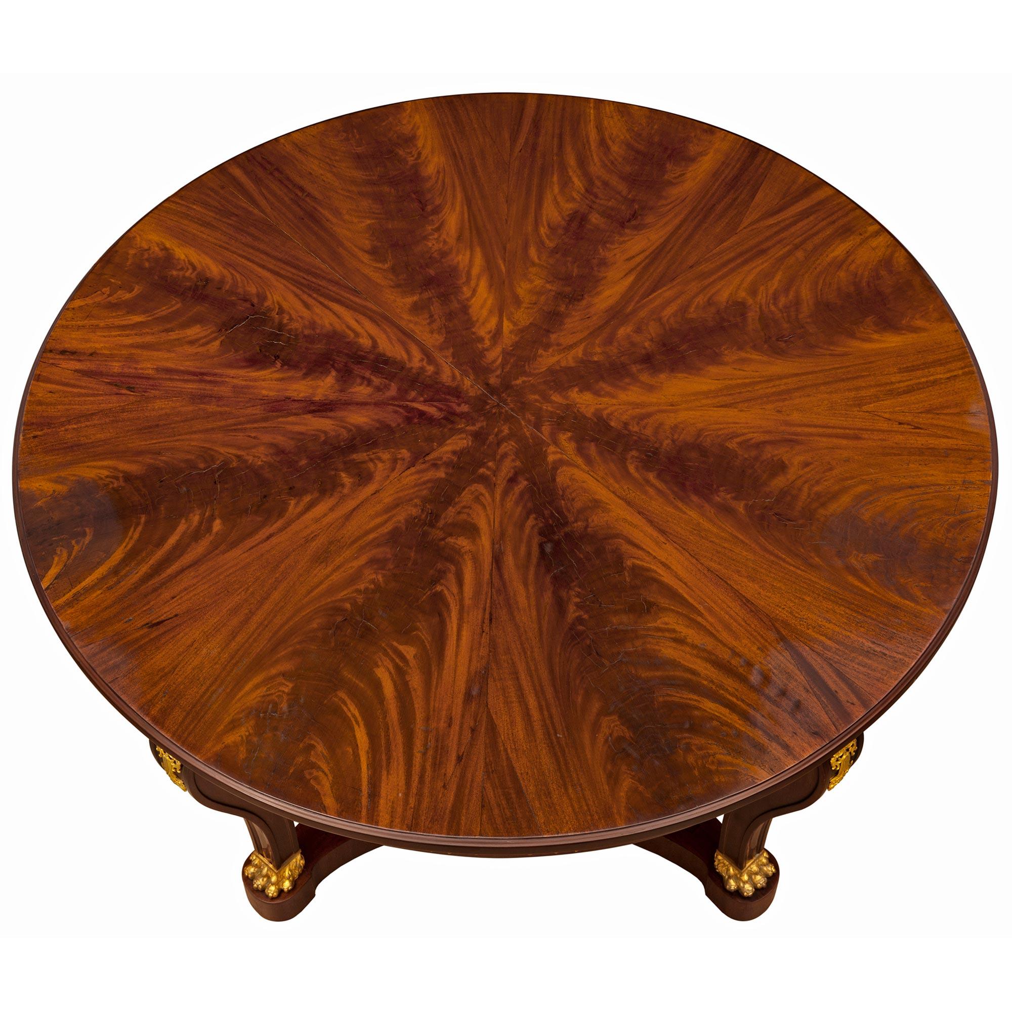 An impressive and most decorative French 19th century Empire St. mahogany and ormolu center table. The circular table is raised by fine bun feet below elegant scrolled legs with handsome ormolu paw feet, recessed carved pierced panels, and foliate