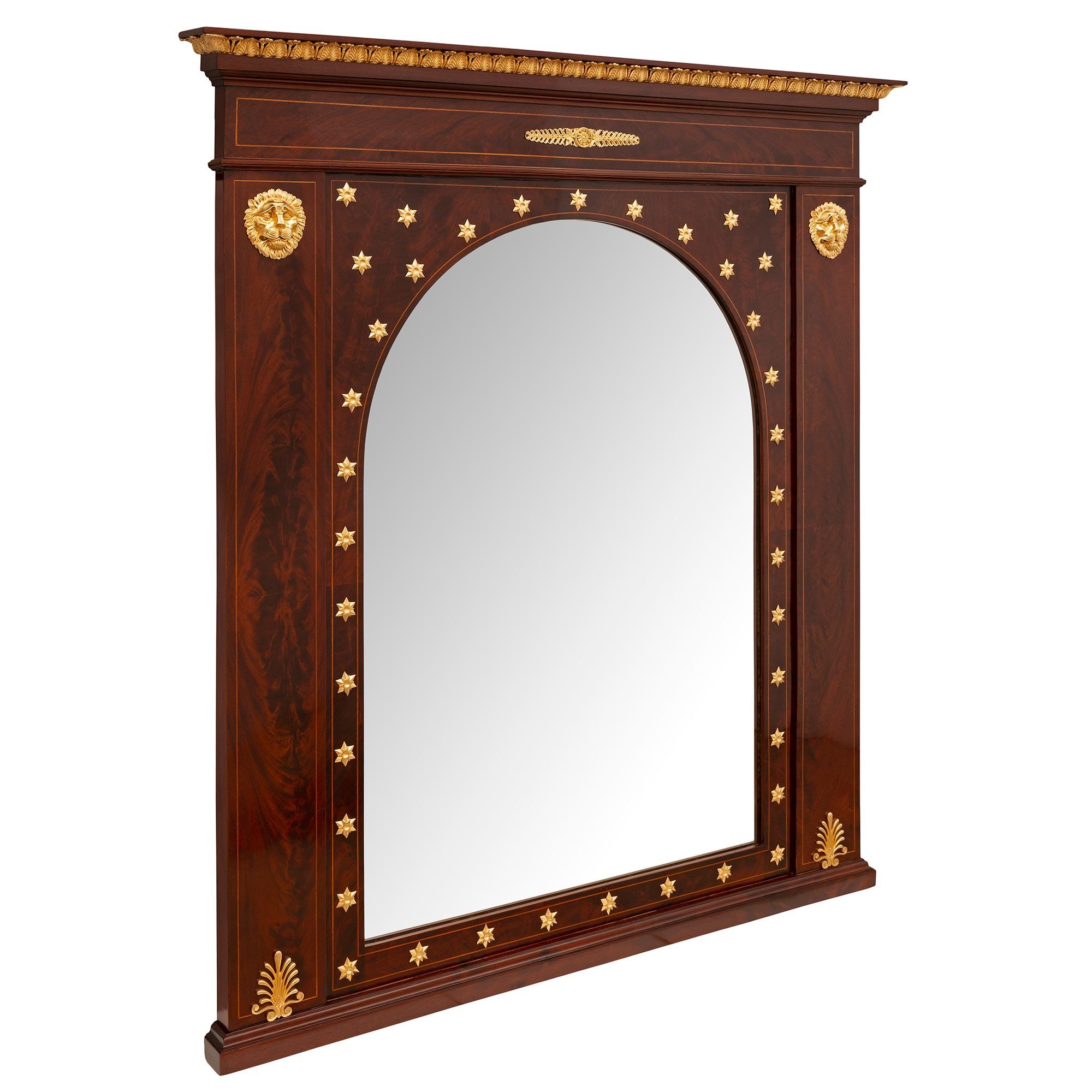 Un impressionnant et unique miroir en acajou et bronze doré de style Empire, datant du 19e siècle. Le miroir est surélevé par une base droite au motif finement marbré. La plaque de miroir centrale d'origine présente un élégant design en forme d'arc