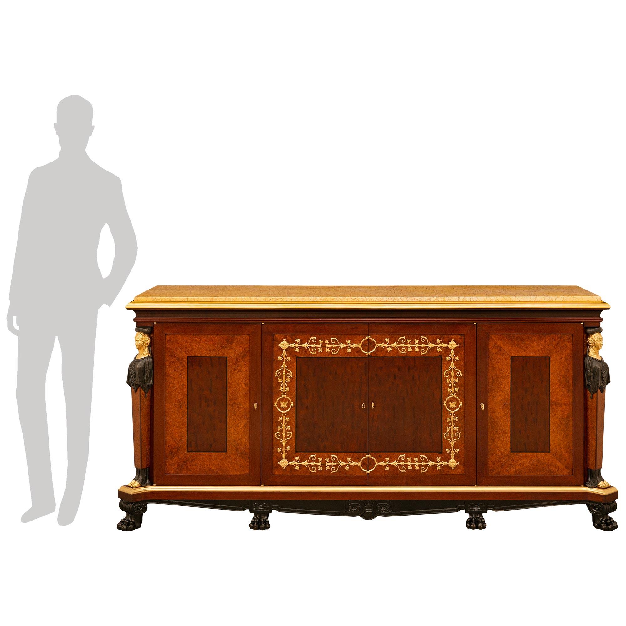 A wonderful and high quality French 19th century Empire st. Mouchette Mahogany, Burl Ash, Santos Mahogany, Kingwood, Ormolu, and Giallo Antico marble buffet. This stunning three drawer four door buffet is supported by eight Ebony paw feet connected