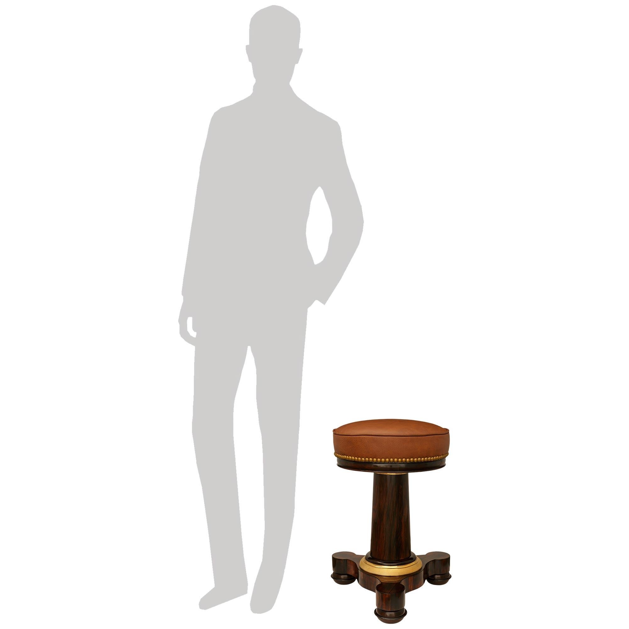 A handsome and high quality French 19th century Empire st. Mahogany, Leather and Ormolu stool. This wonderful swivel stool is raised on triangular Mahogany base with three protruding bun feet surrounding the circular Mahogany base. Above is an