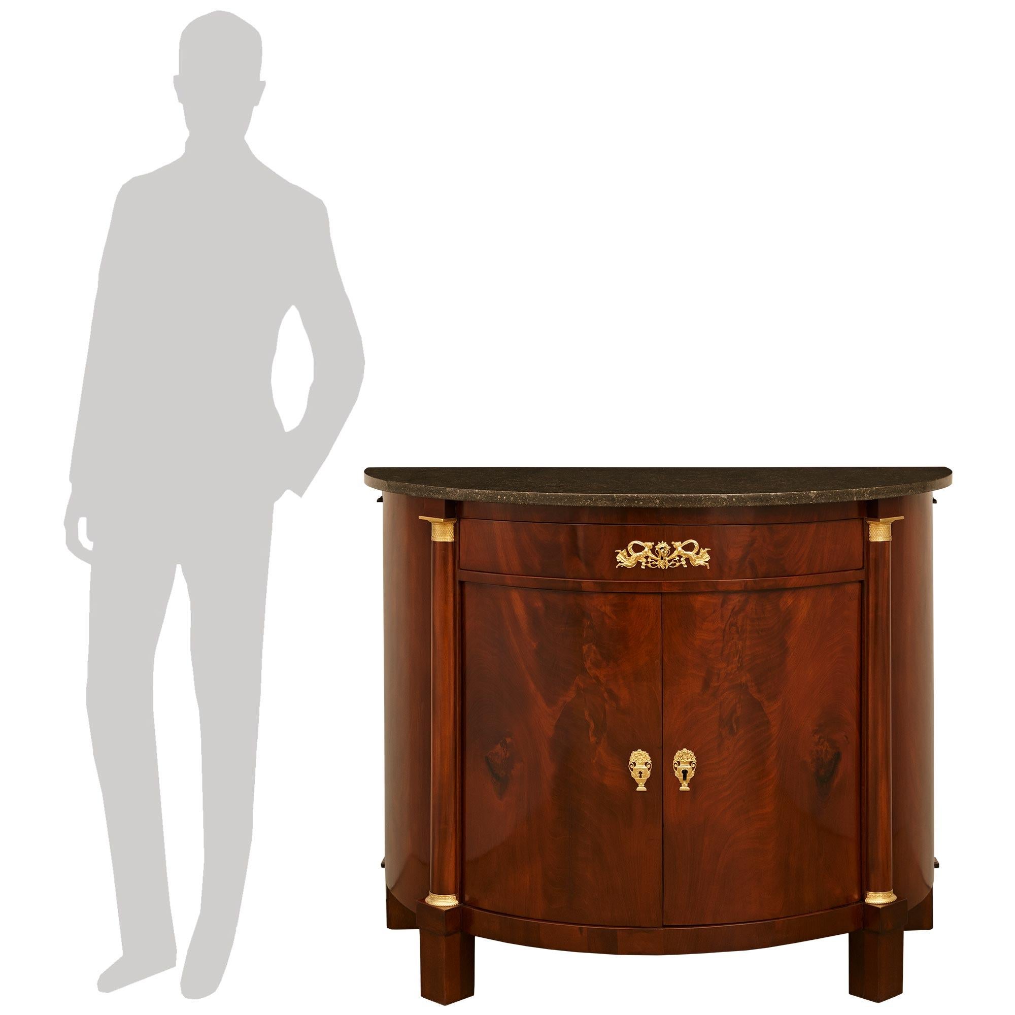 Hermoso mueble de caoba, ormolu y mármol fosilizado del siglo XIX, de estilo Imperio francés y de gran calidad. Este maravilloso mueble en forma de demi luna se alza sobre cuatro patas de bloque de caoba que sostienen el faldón en forma de D. En el