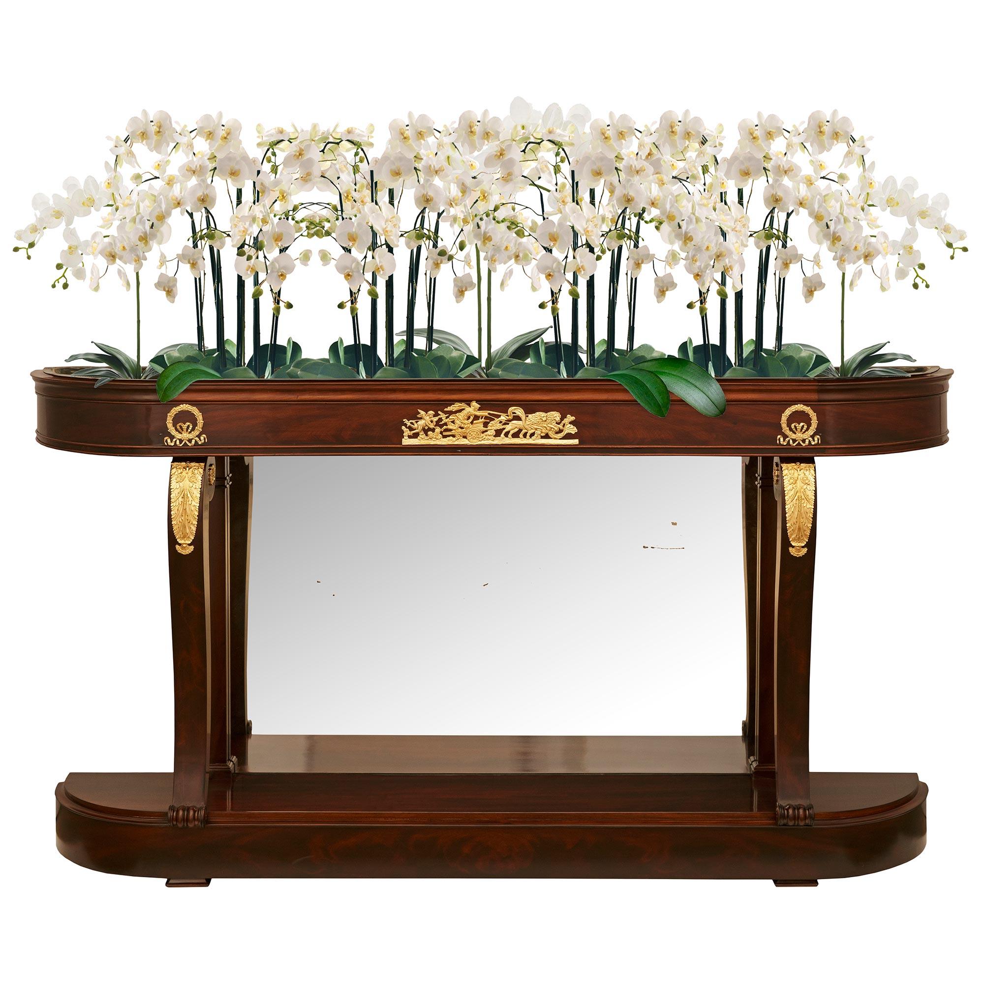 An elegant and most unique French 19th century Empire St. Mahogany, Ormolu and Mirror planter/console. This exquisite freestanding elongated demi lune console is raised by on thick flame Mahogany plinth. At the front are two scrolled supports
