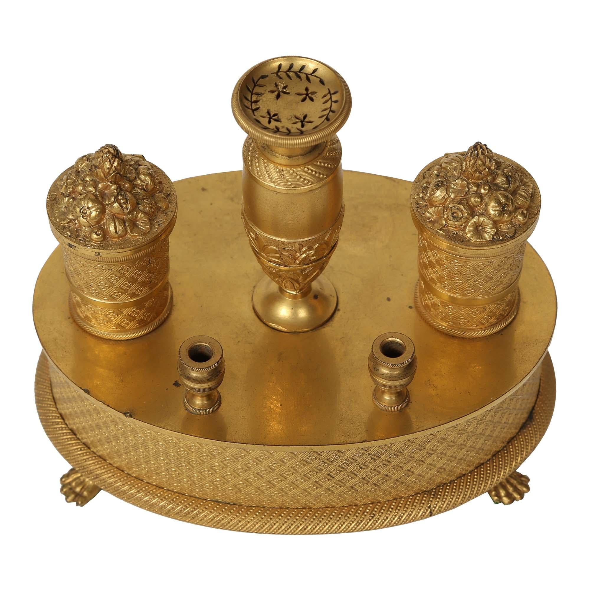 An exquisite French 19th century Empire st. oval ormolu inkwell. The inkwell is raised by pawed feet below a lattice design with rosettes in the center. Above are two ink dispensers with lids in the shape of flower and fruit baskets. At the center