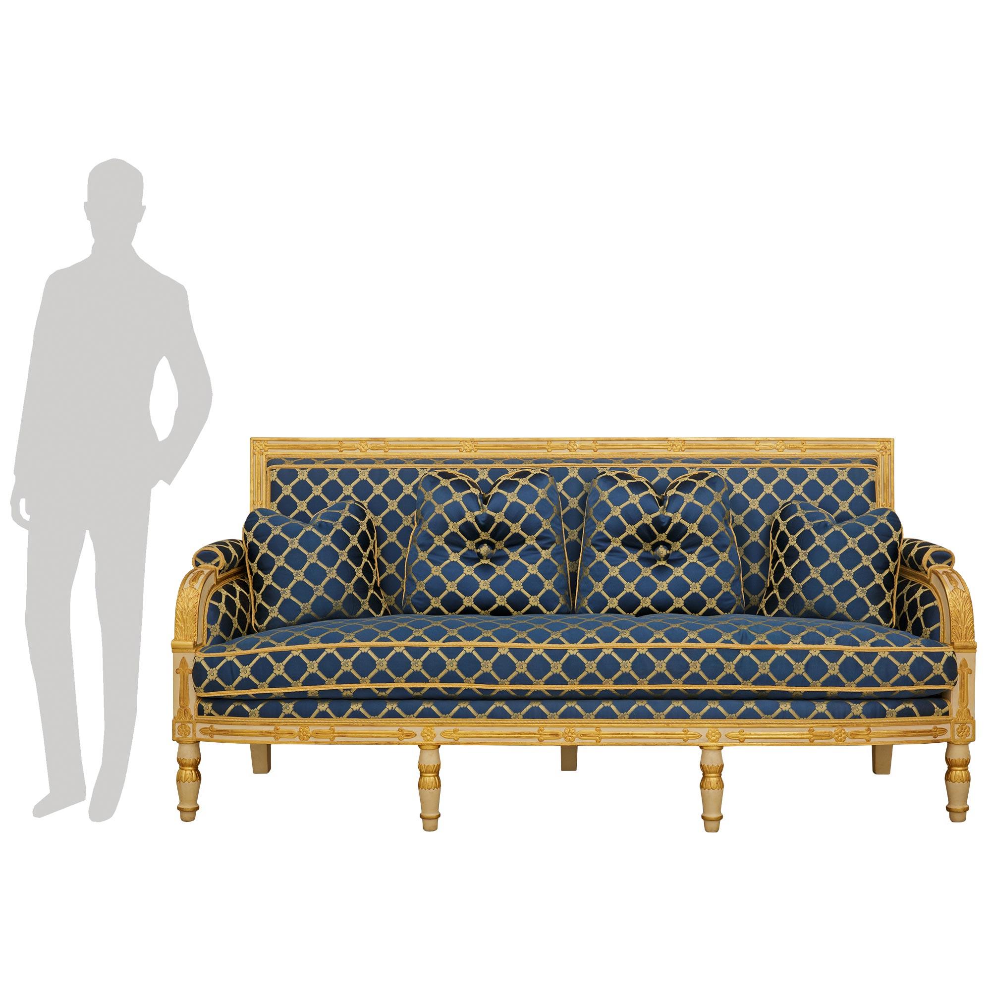 Sofá de madera patinada y giltwood del siglo XIX, de estilo Imperio francés. Este excepcional canapé se eleva sobre siete soportes, cuatro de los cuales son patas delanteras circulares con base y rematadas con bandas de madera dorada, y un diseño