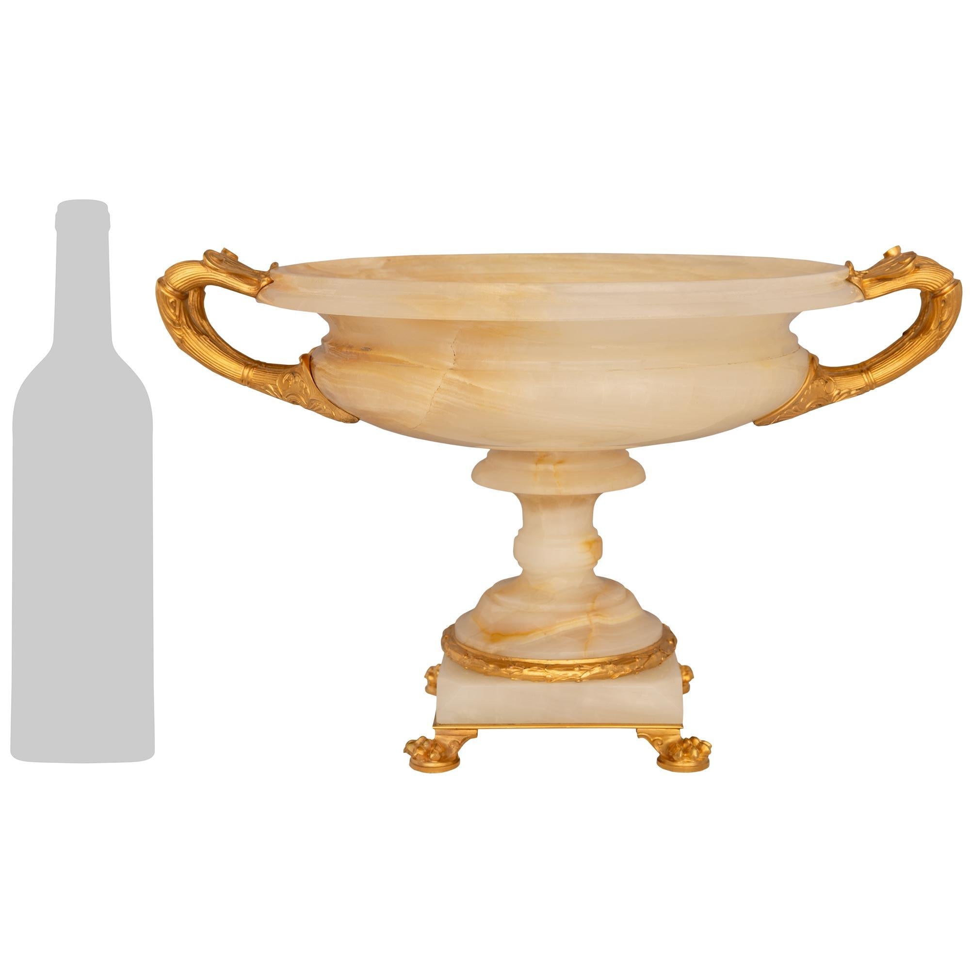 Impressionnant centre de table en onyx blanc et bronze doré de haute qualité, datant du XIXe siècle et de style Empire. Ce magnifique centre de table/tazza repose sur une base carrée en onyx enveloppée d'une bande de laurier et soutenue par une