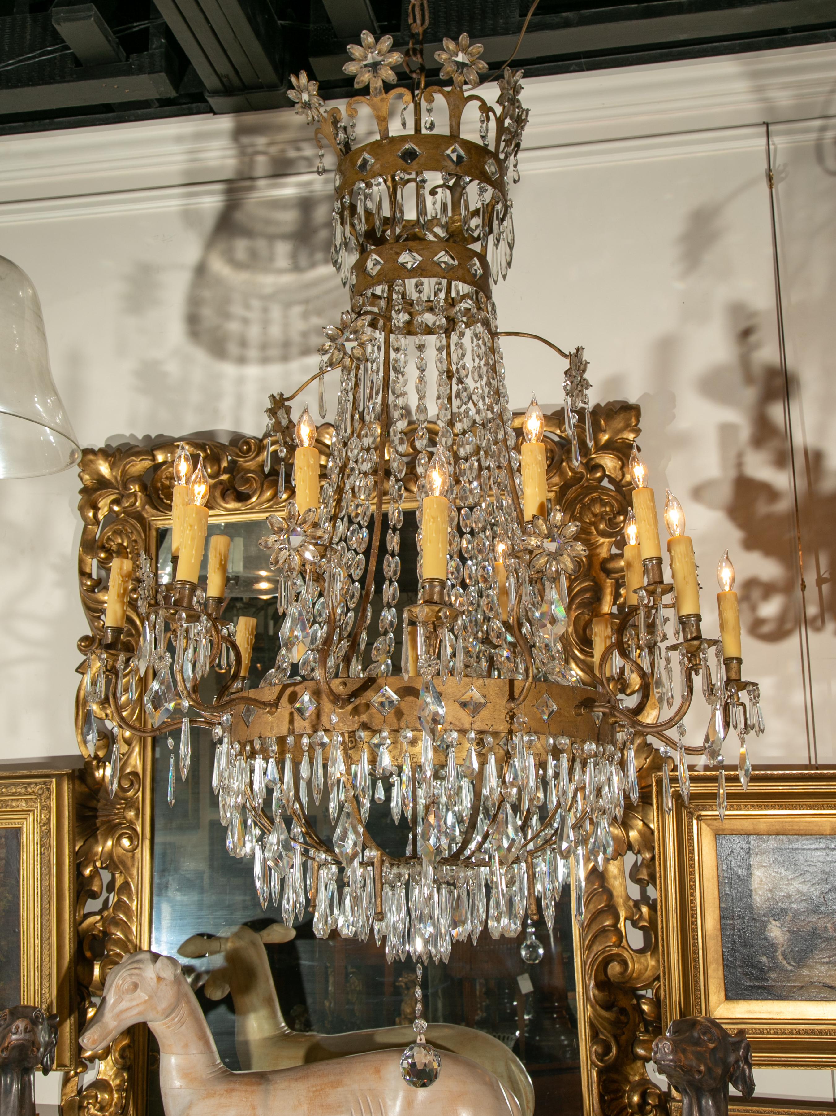 Grande lampadario a 16 luci in cristallo e metallo dorato in stile Impero francese del XIX secolo, con bracci a spirale, motivi a diamante e a rosetta. Nato in Francia durante il dinamico XIX secolo, questo lampadario è caratterizzato da una serie