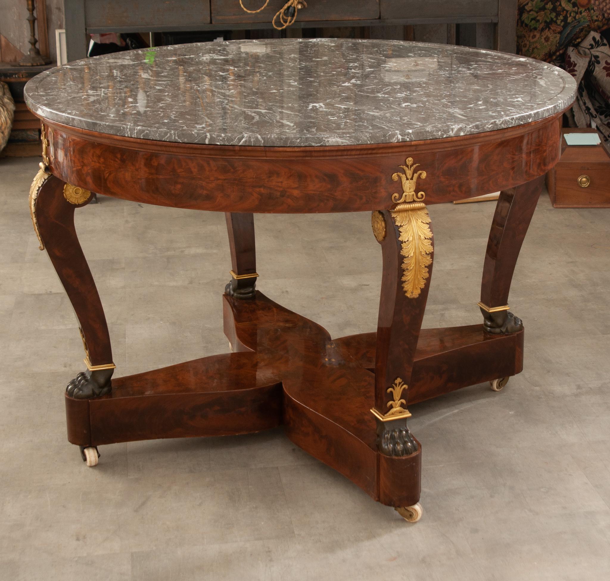 An impressive 19th Century Empire center table made in France. The gray-white marble top sits perfectly on its table base with an inset beveled marble ring. The table base is wrapped in stunning flame mahogany and is raised by elegant scrolled legs