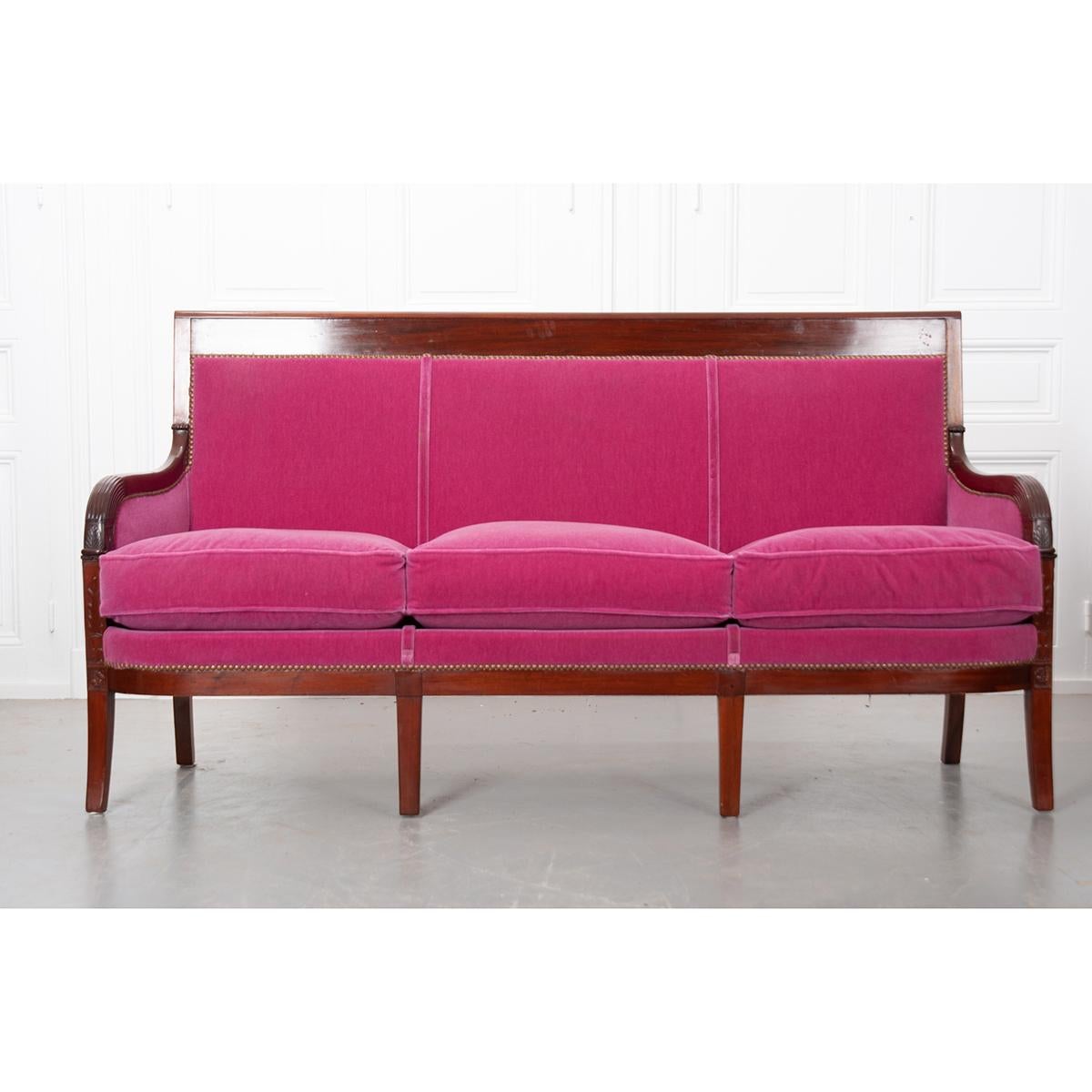 Upholstered in a fabulous pink velvet with nail-head trim, this 19th century Empire-style settee is ready to be added to your space. Its solid mahogany frame has a rich, deep color and features hand carved details on the arms extending onto the two
