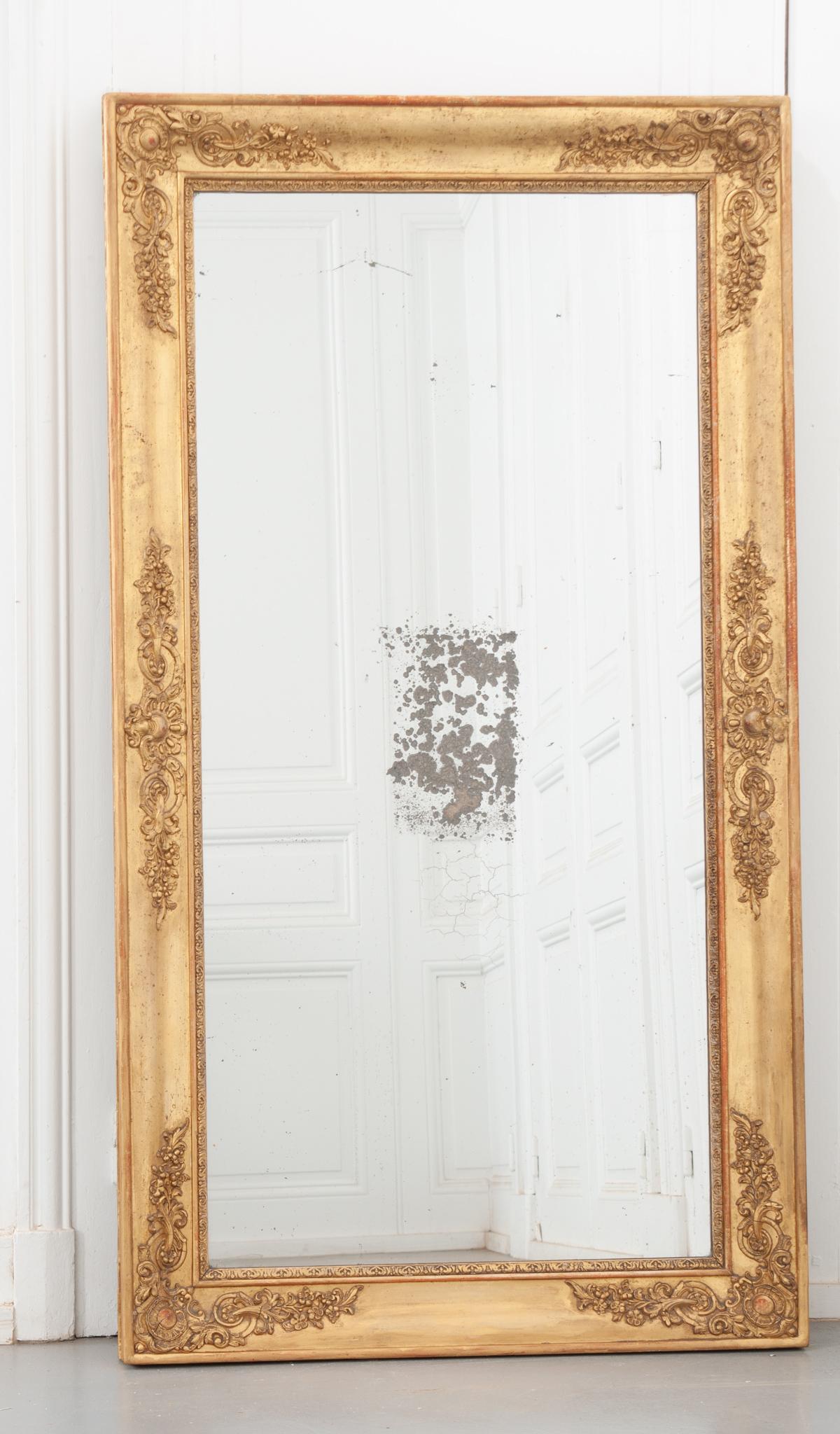 This beautiful Empire style mirror is dripping with exceptional details. The giltwood frame has a fantastic patina throughout, with spots of French red peaking through. Detailed motifs depicting a crest and lush flowered vines embellish the frames