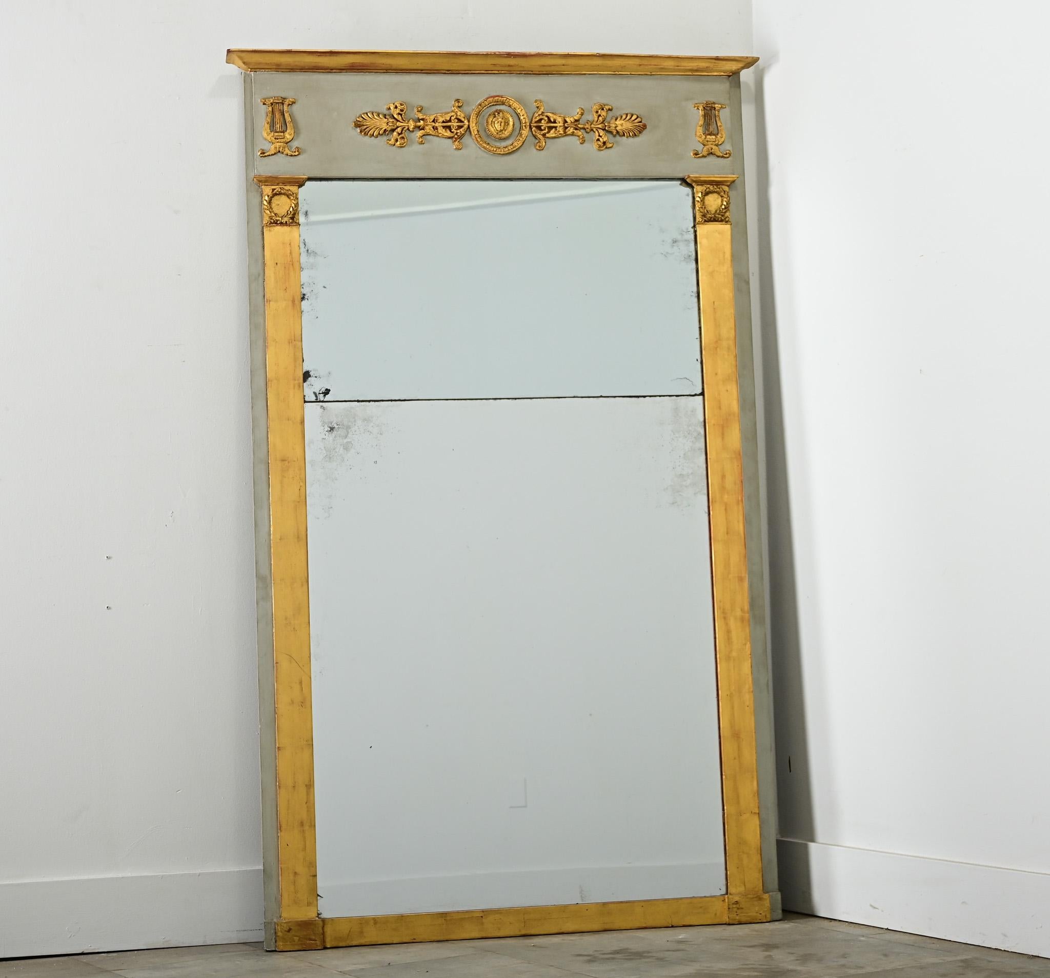 Un gran espejo trumeau Imperio francés del siglo XIX, audaz pero refinado, que utiliza elementos decorativos neoclásicos para proyectar respeto por la historia y el lujo. En el friso de la parte superior, sobre el marco de madera pintada de color