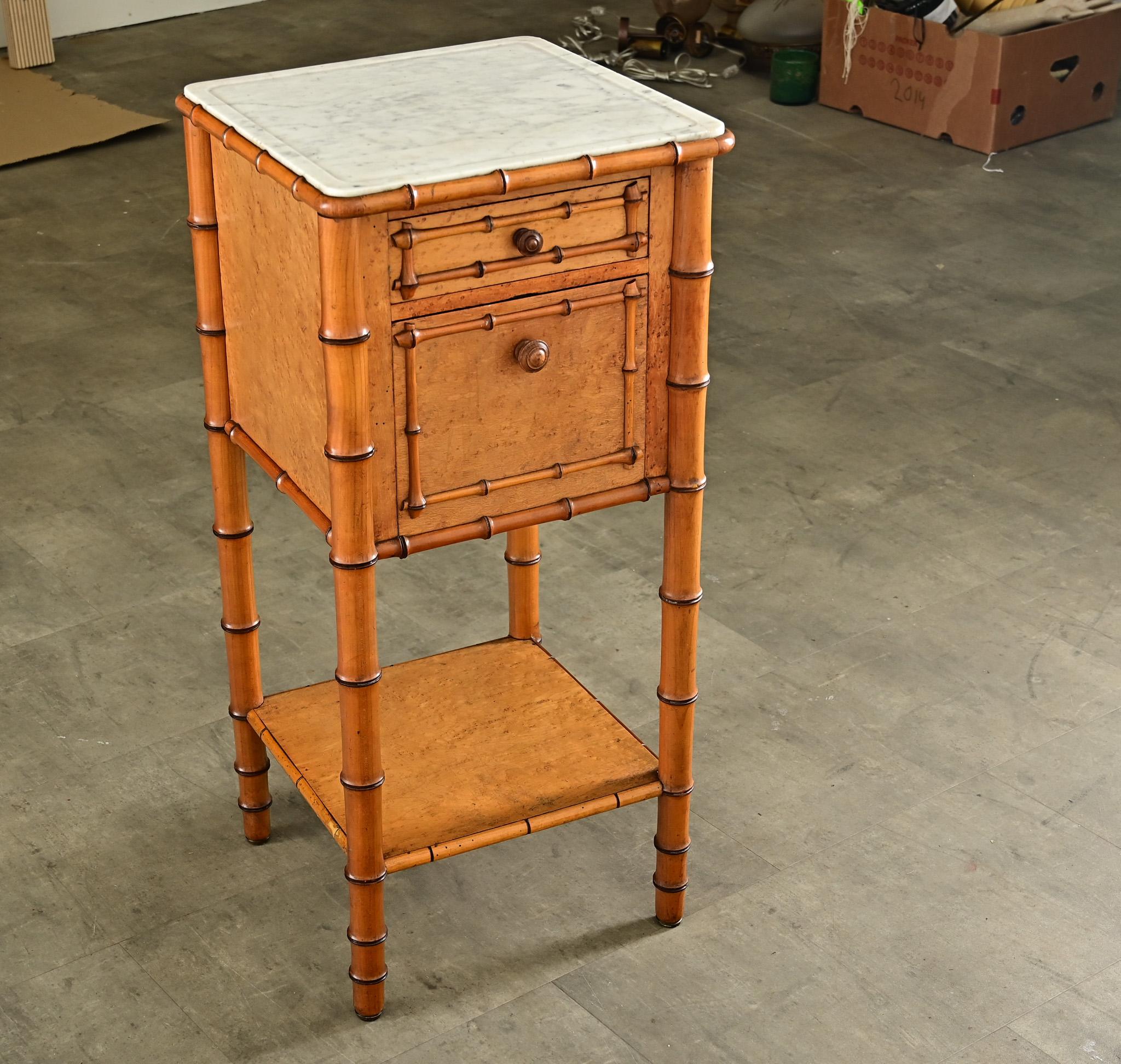 A delightful faux-bamboo bedside table from late 19th century France in carved pine and maple. The top surface is white marble, shaped with a dish top forming a lip around the perimeter and rounded at the corners. Below is a small, shallow drawer