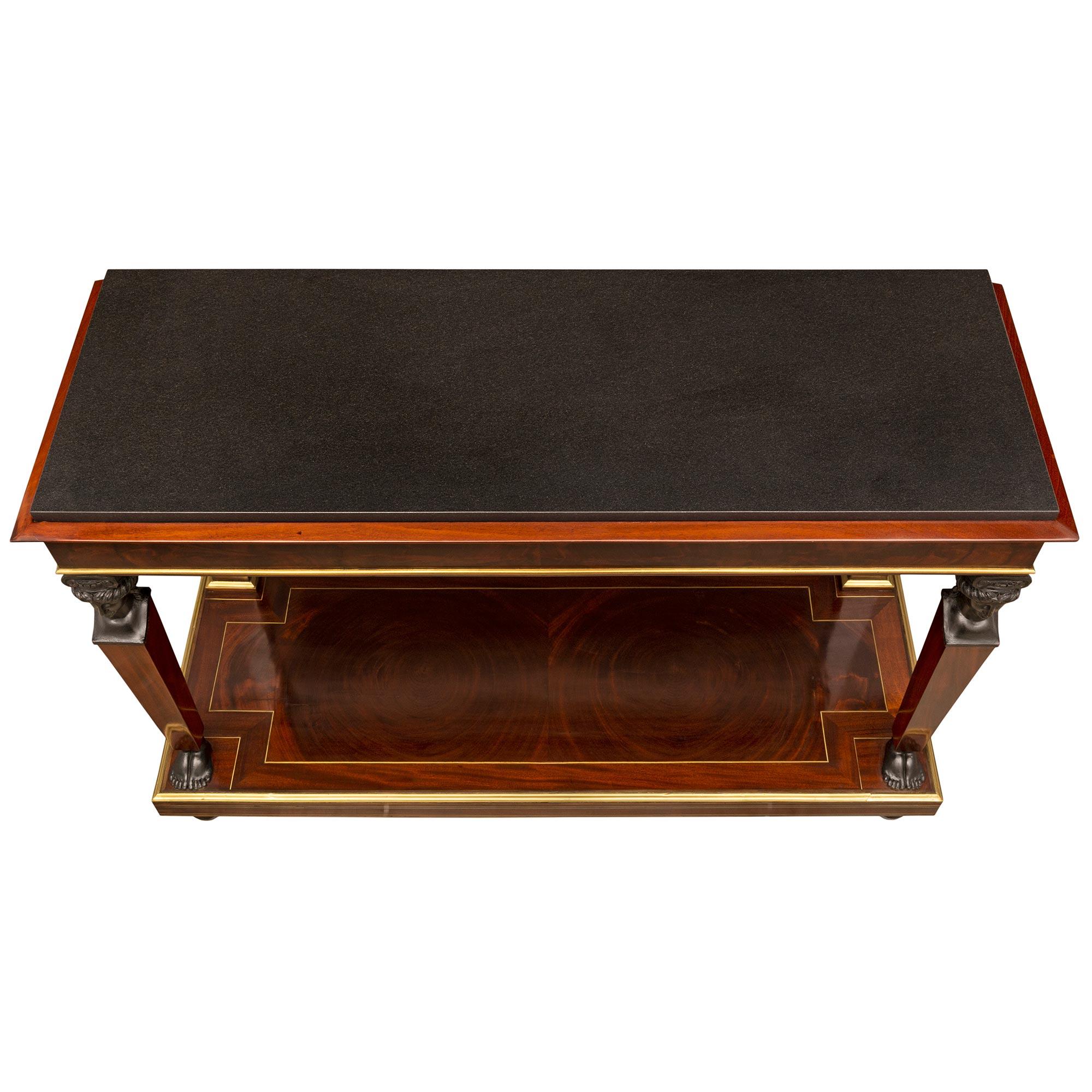 A striking French early 19th century 1st Empire period flamed mahogany, ebonized fruitwood, brass and black Belgian marble console. The two tiered freestanding console is raised by fine ball feet with most decorative brass fillets extending along