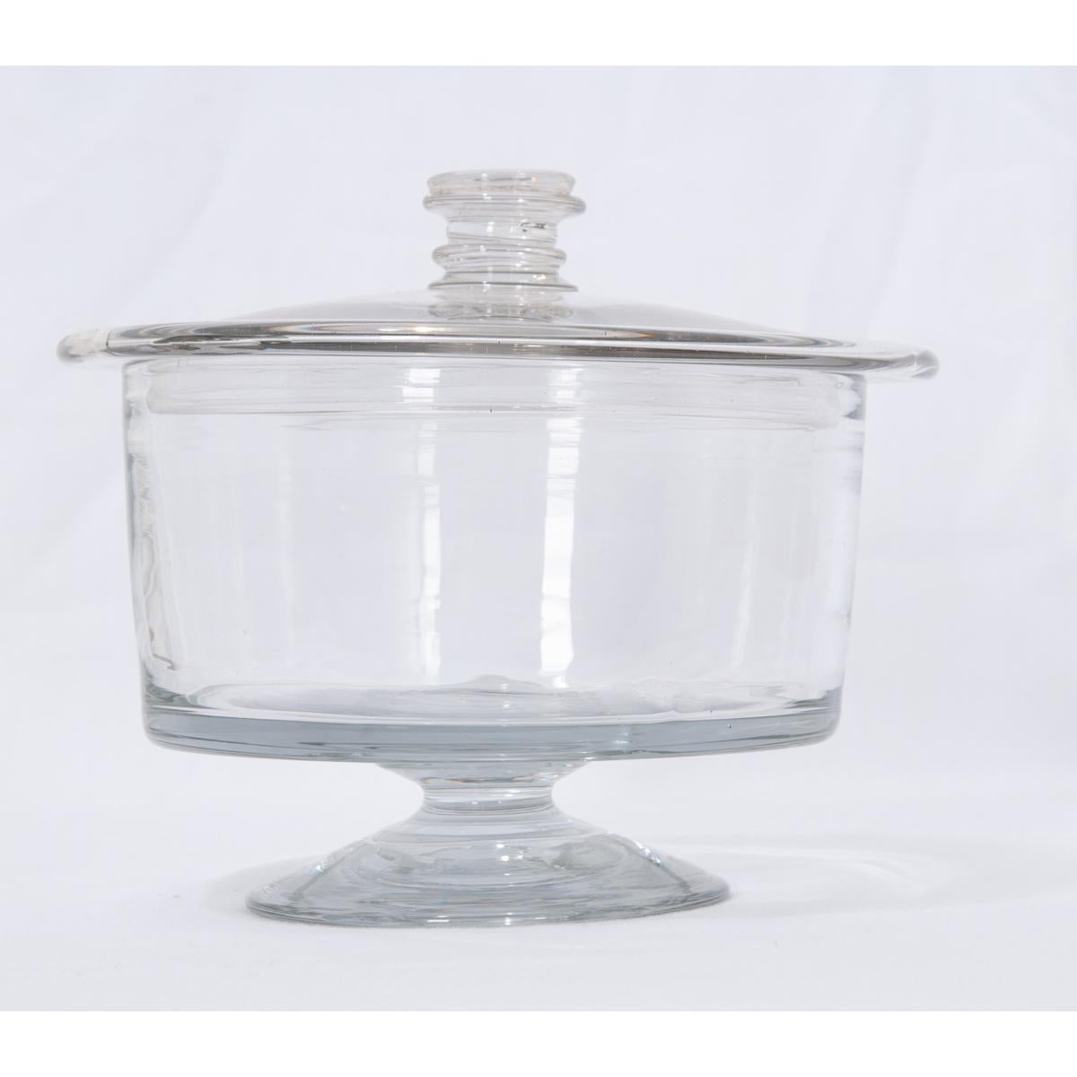 Petite, clear glass jar with lid. This sweet little jar is raised on a short pedestal and is crowned with a flat lid. The lid overhangs the jar and has a ‘turned liked’ handle topping it off.