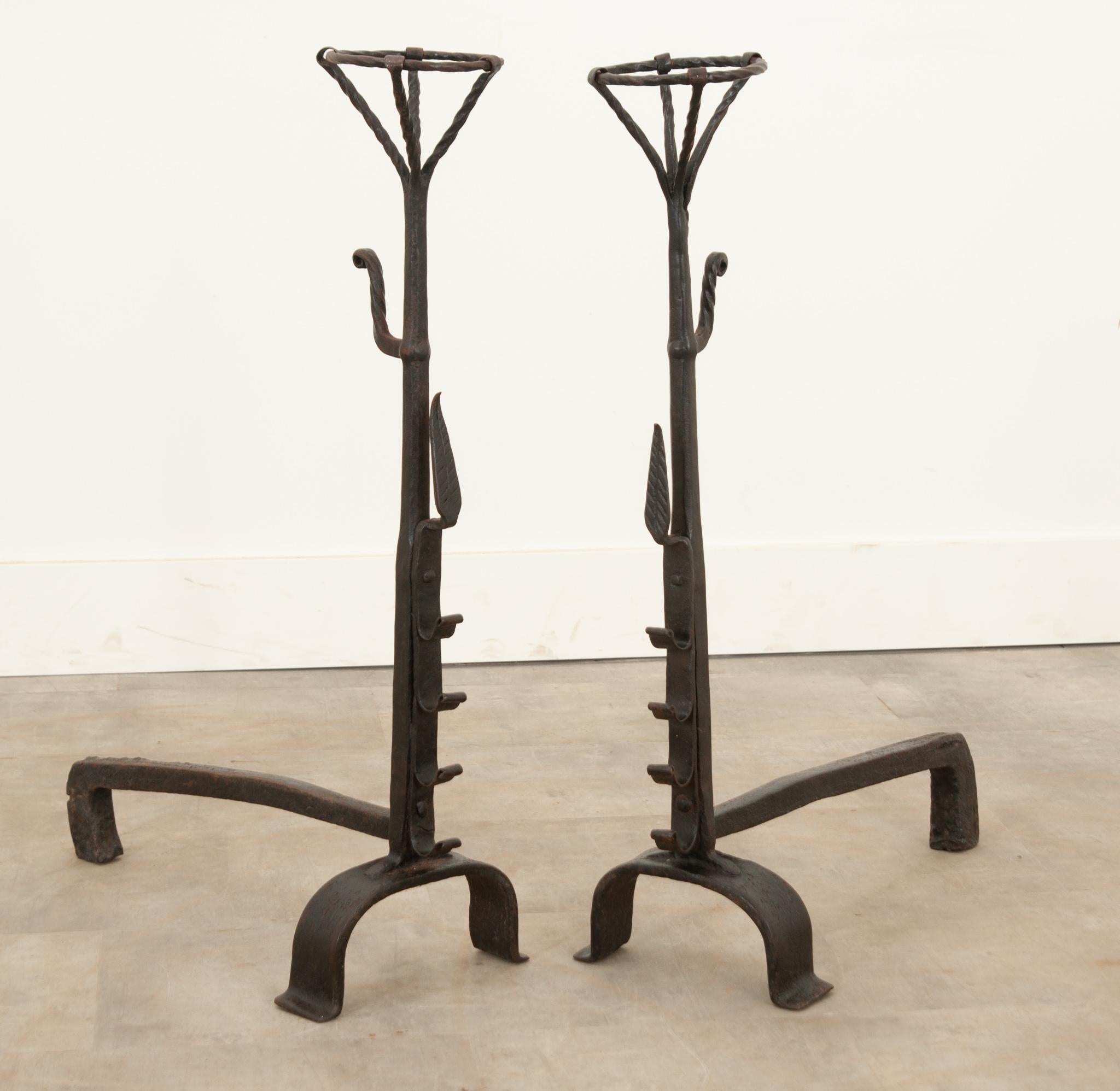 This pair of hand forged iron andirons come from 19th century France. Used to support logs, these L shaped brackets are simply constructed. A unique detail on the front of the andirons, a forged notches dedicated for roasting sticks to cook over the