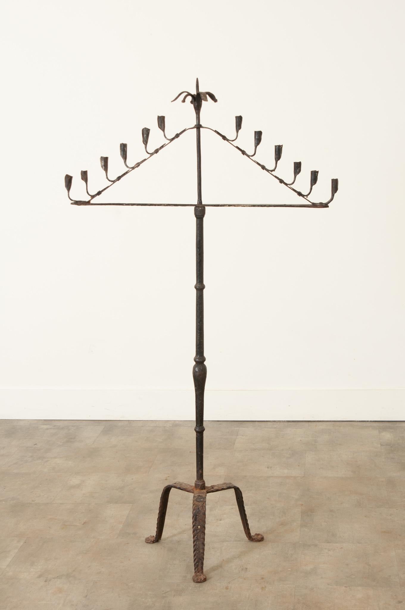 A fabulous 19th Century hand-forged iron candelabra, made in France circa 1840. Beautifully designed, this fixture will hold six candles in its graceful, fluted candle cups that resemble calla lilies and a larger 13th candle may be placed in its