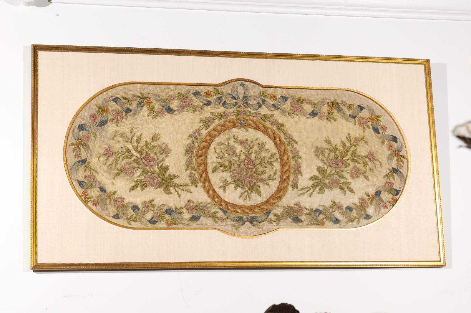A French framed needlepoint tapestry from the 19th century, with ribbon and floral motifs. Set inside a simple yet elegant gilded frame with matting and gilt rim, this lovely horizontal needlepoint tapestry features an oblong shape accented with a