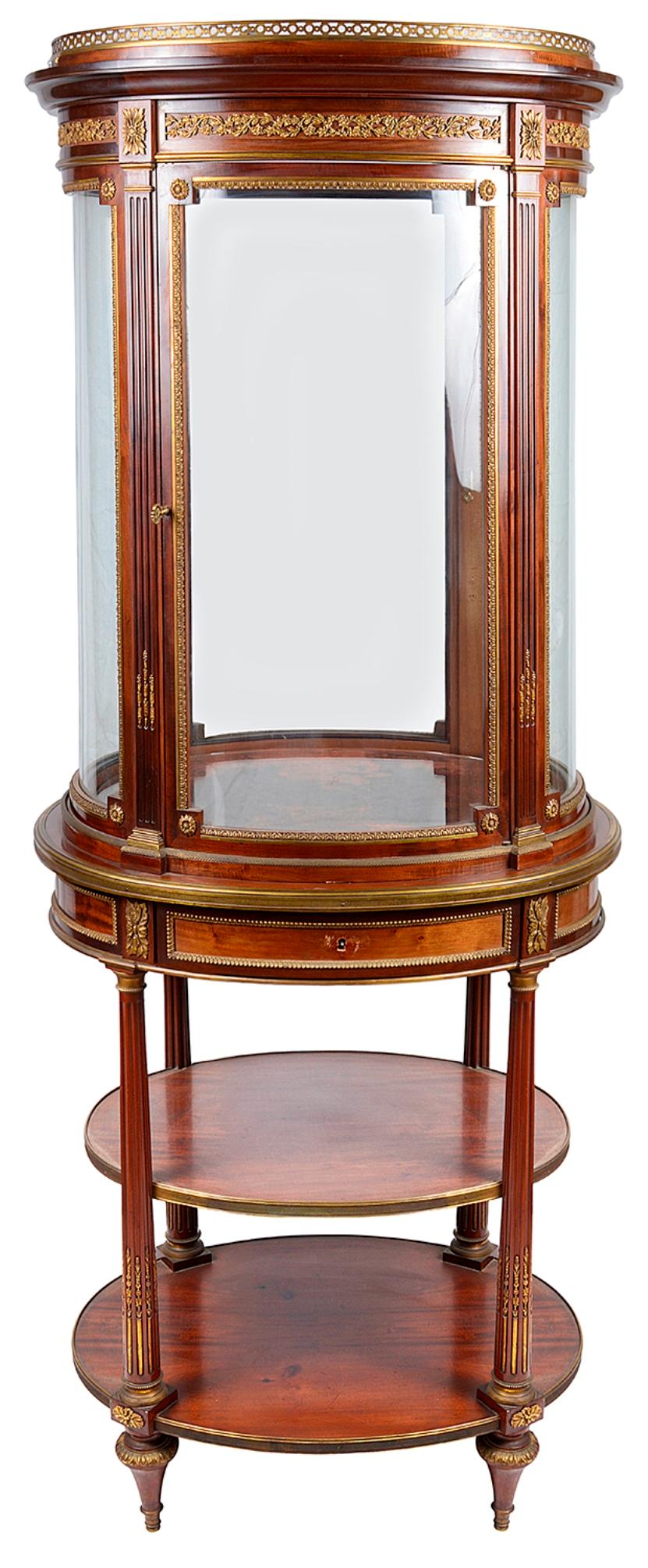 A very good quality late 19th century French mahogany free standing oval vitrine, having a gilded ormolu gallery to the top and foliate mounts to the pelmet. Bowed glass panels to all sides, a single door opening to reveal glass shelves within. A