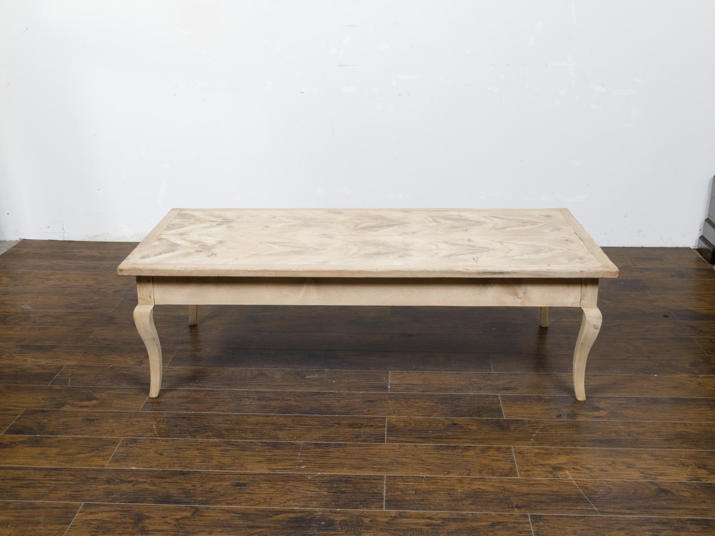 A French Louis XV style bleached fruitwood coffee table from the 19th century with butterfly veneer and carved cabriole legs. This elegant French Louis XV style coffee table, crafted in the 19th century from fruitwood, beautifully exemplifies the