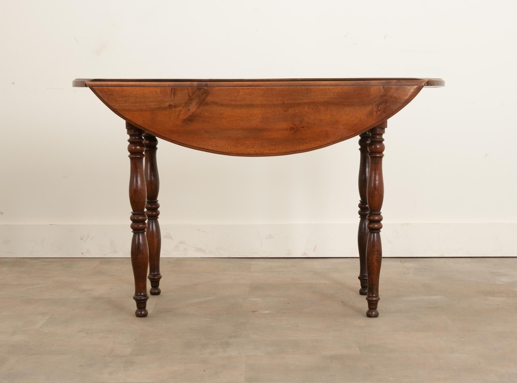 A lovely French 19th century drop leaf dining table crafted from solid fruitwood. The top sits over a simple apron supported with four wonderfully turned legs. Each drop leaf has a wood support that pulls out with an iron handle from under the