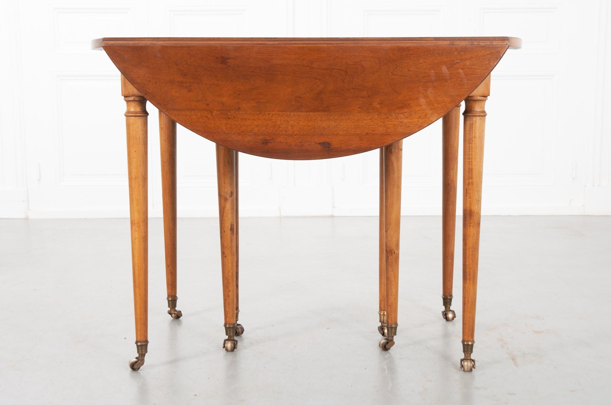 A lovely French 19th century drop leaf extending dining table. The fruitwood has a nice warm patina. The top sits over a simple apron supported with four tapered legs on brass caps with brass casters. There are four legs, also on casters, in the