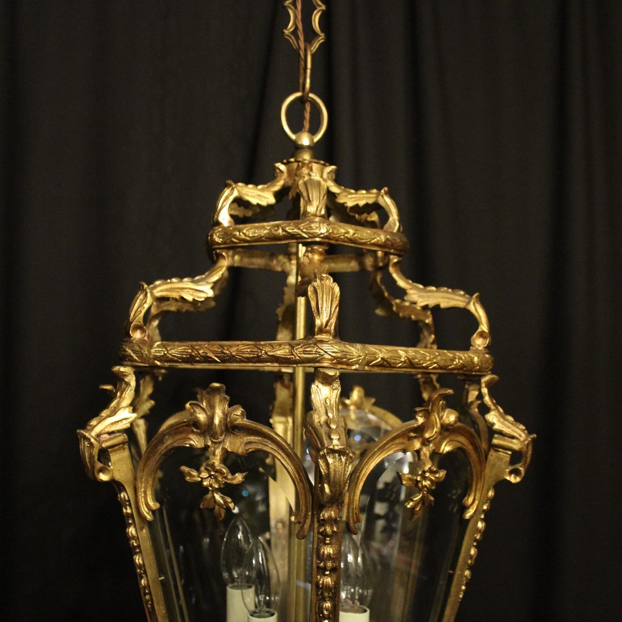 A French late 19th century gilded bronze four-light hexagonal antique hall lantern, the six original beveled glass panels held within an ornate scrolling framework with four light fittings and having decorative scrolled inverted floral central leaf