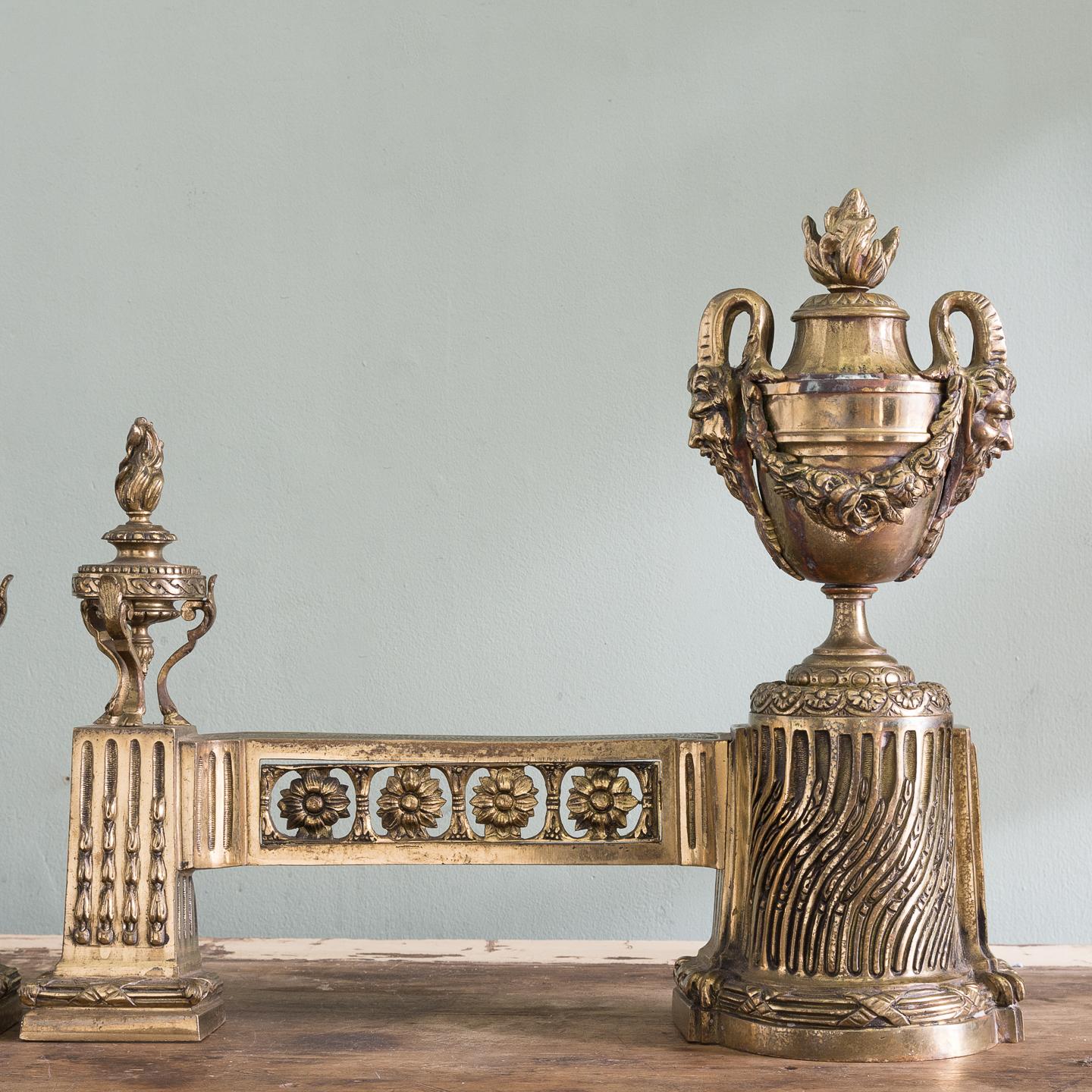 A pair of 19th century French chenets, gilded bronze, in the neoclassical taste, each with large flaming classical urn with Satyr mask handles with garlands hung between, raised on strigilated plinth, the horizontal supports with paterae details