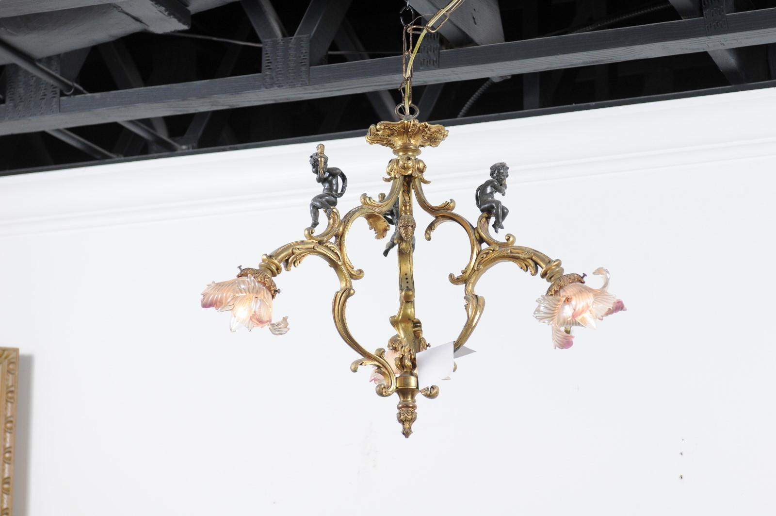 A French gilt bronze three-light chandelier from the 19th century, with three putti holding torches and hand-blow glass bobèches. Born in France during the 19th century, this three-arm chandelier captures our attention with its Rococo curves and