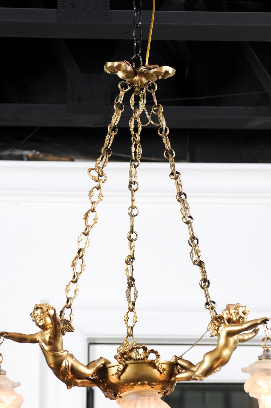 A French gilt metal three-light chandelier from the 19th century, with ribbons and cherubs holding the shades. Born in France during the 19th century, this three-light chandelier features a ribbon-tied canopy, supporting profiled links. The lower