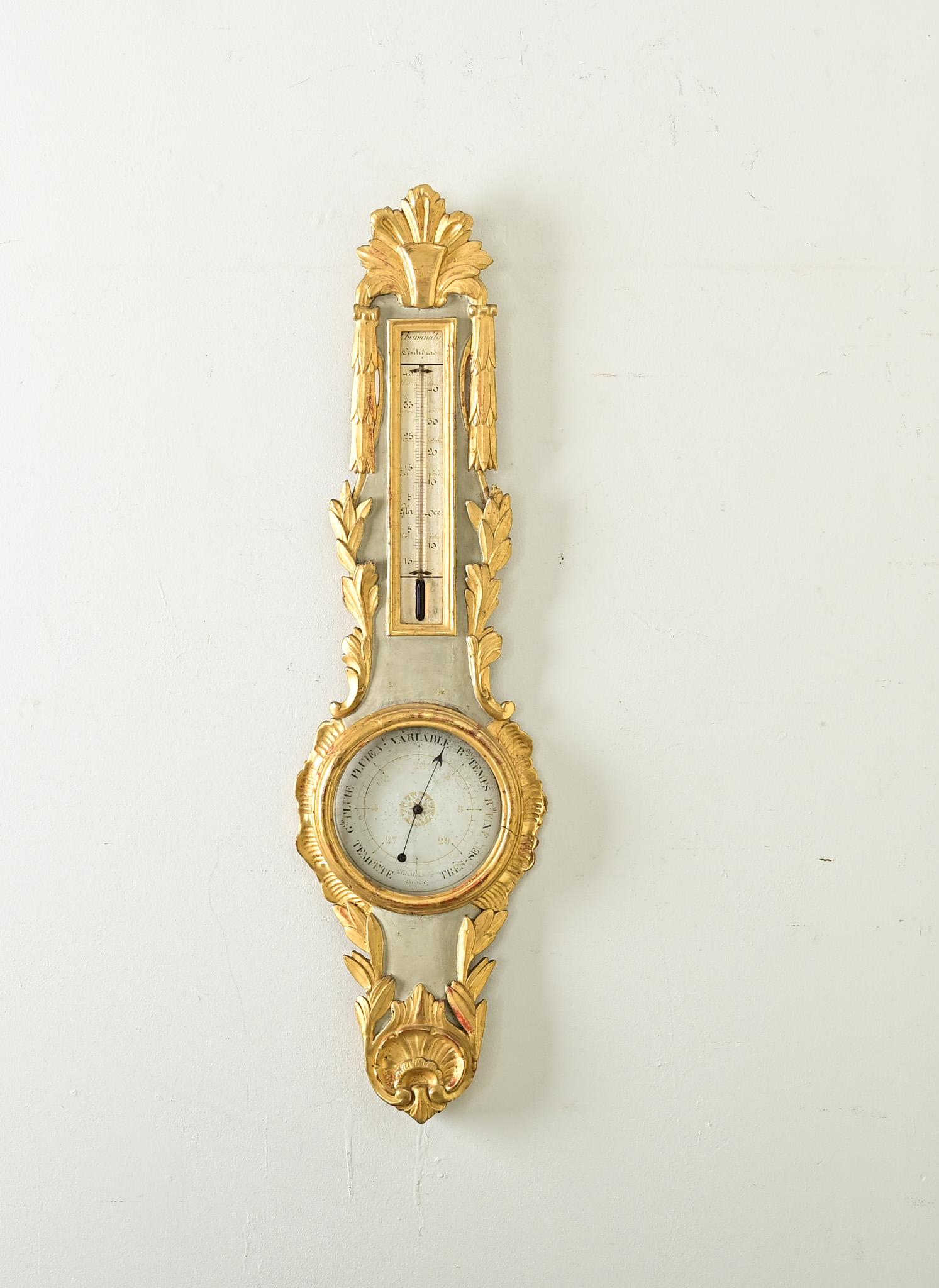 A gorgeous French 19th century painted and gold gilt barometer with thermometer. The elegantly carved giltwood surrounding the French gray-painted case is in a rococo and laurel leaf theme–a lovely contrast to the intention as a scientific