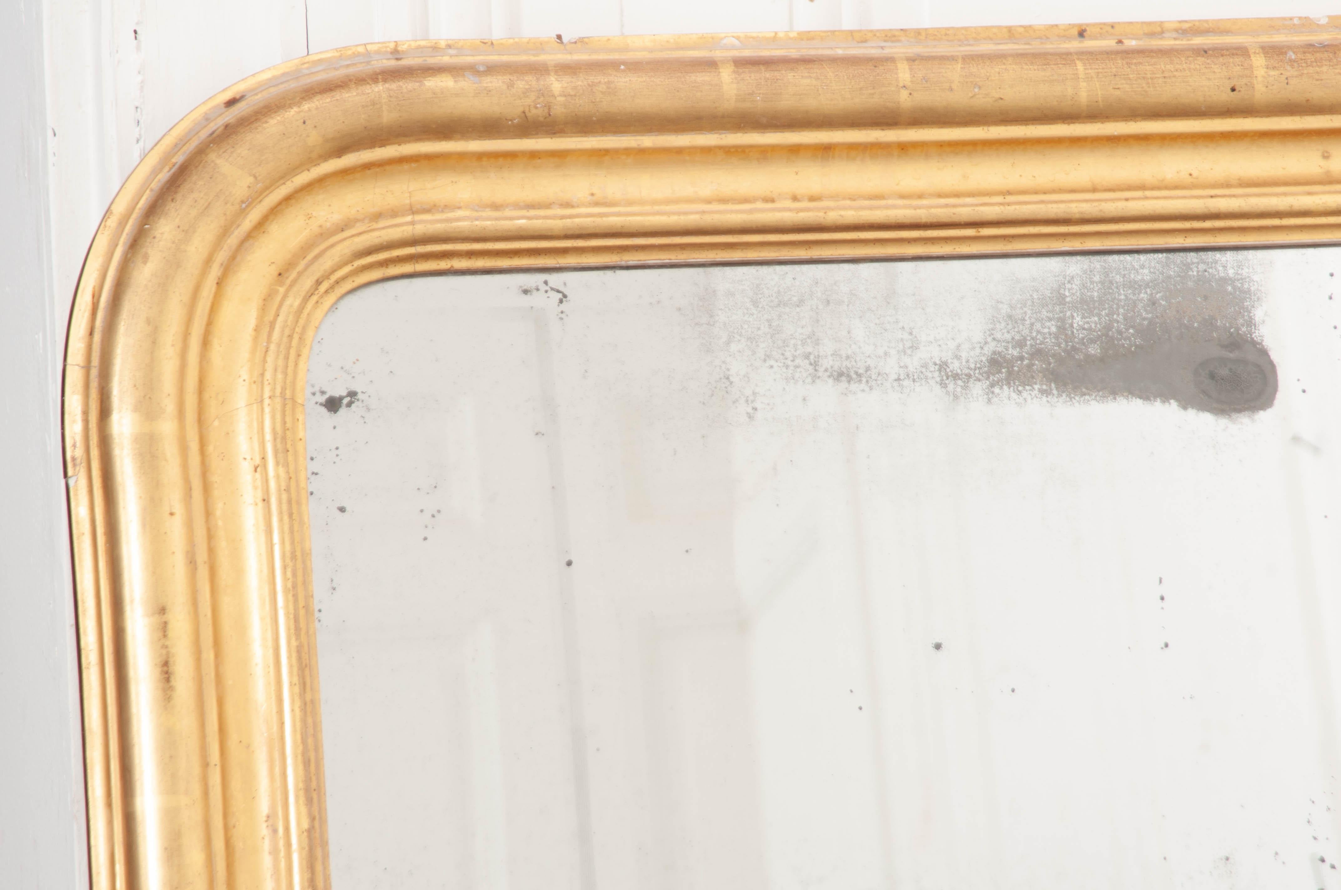 A generously proportioned gold giltwood Louis Philippe mirror from 19th century, France. The classically-formed mirror has the familiar Louis Philippe silhouette: linear sides and bottom, with curved top corners. This mirror’s frame is carved in a