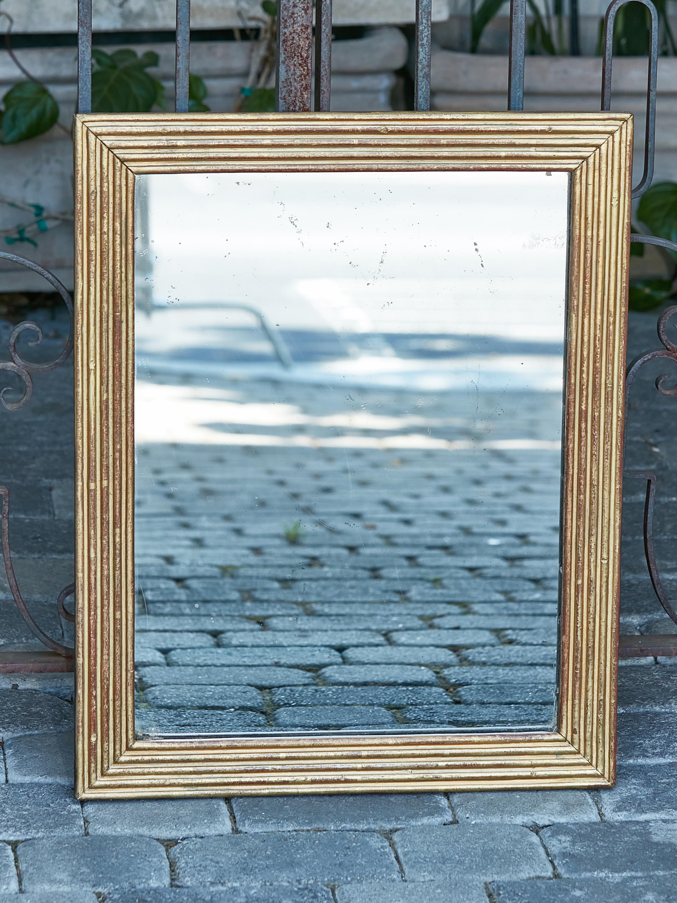 A French giltwood rectangular mirror from the 19th century with reeded décor. Introducing a piece of French artistry, this 19th-century giltwood rectangular mirror captures the essence of classic European elegance. With its simply adorned frame and