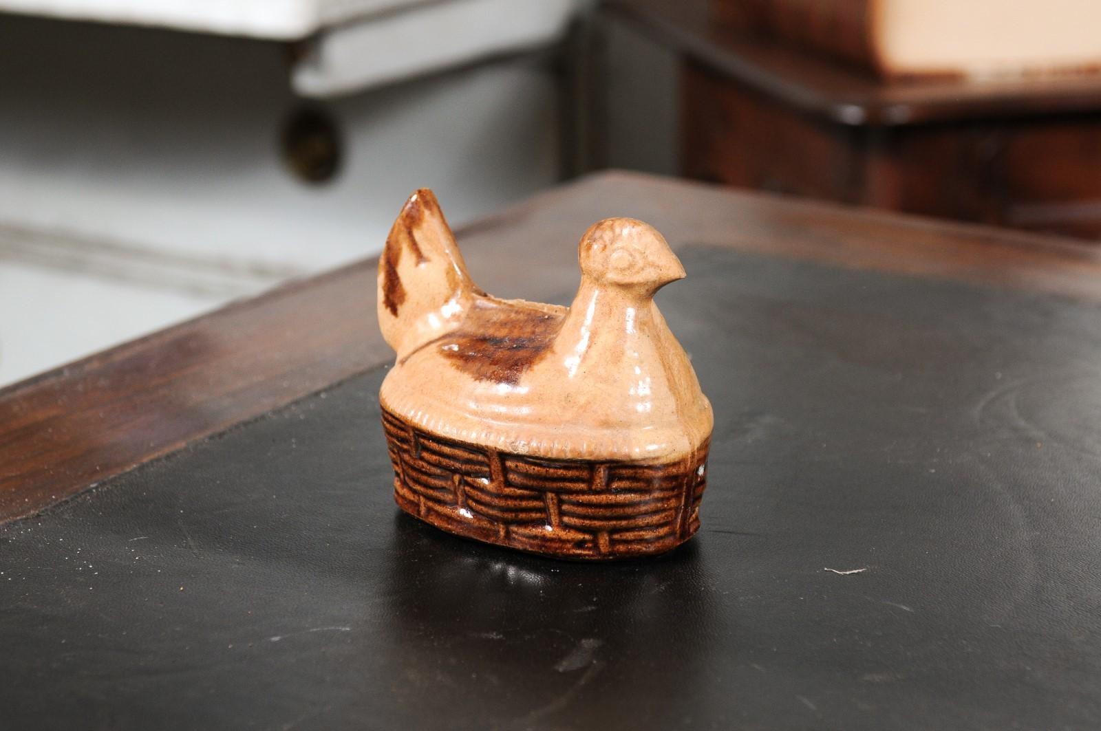 A French glazed majolica chicken bank from the 19th century, with wicker style base. Created in France during the 19th century, this glazed majolica bank depicts a chicken laying on a wicker style base. Boasting brown and cream tones, this 19th