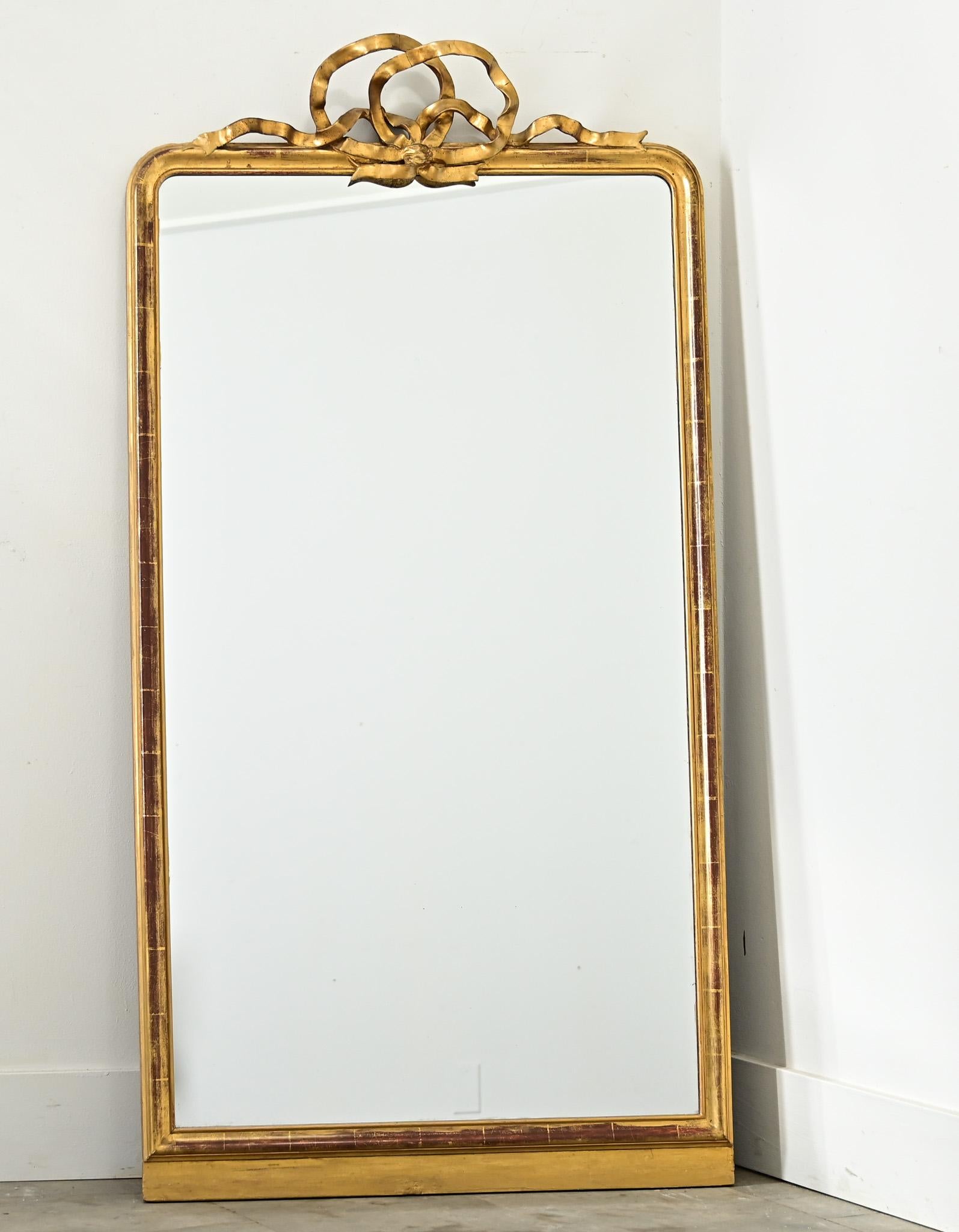 Specchio da camino francese del XIX secolo in oro dorato, la silhouette altrimenti sobria della cornice con angoli arrotondati alla Louis Philippe è stata coronata da un delicato stemma a nastro, più in linea con la tradizione Louis XVI. Due anelli