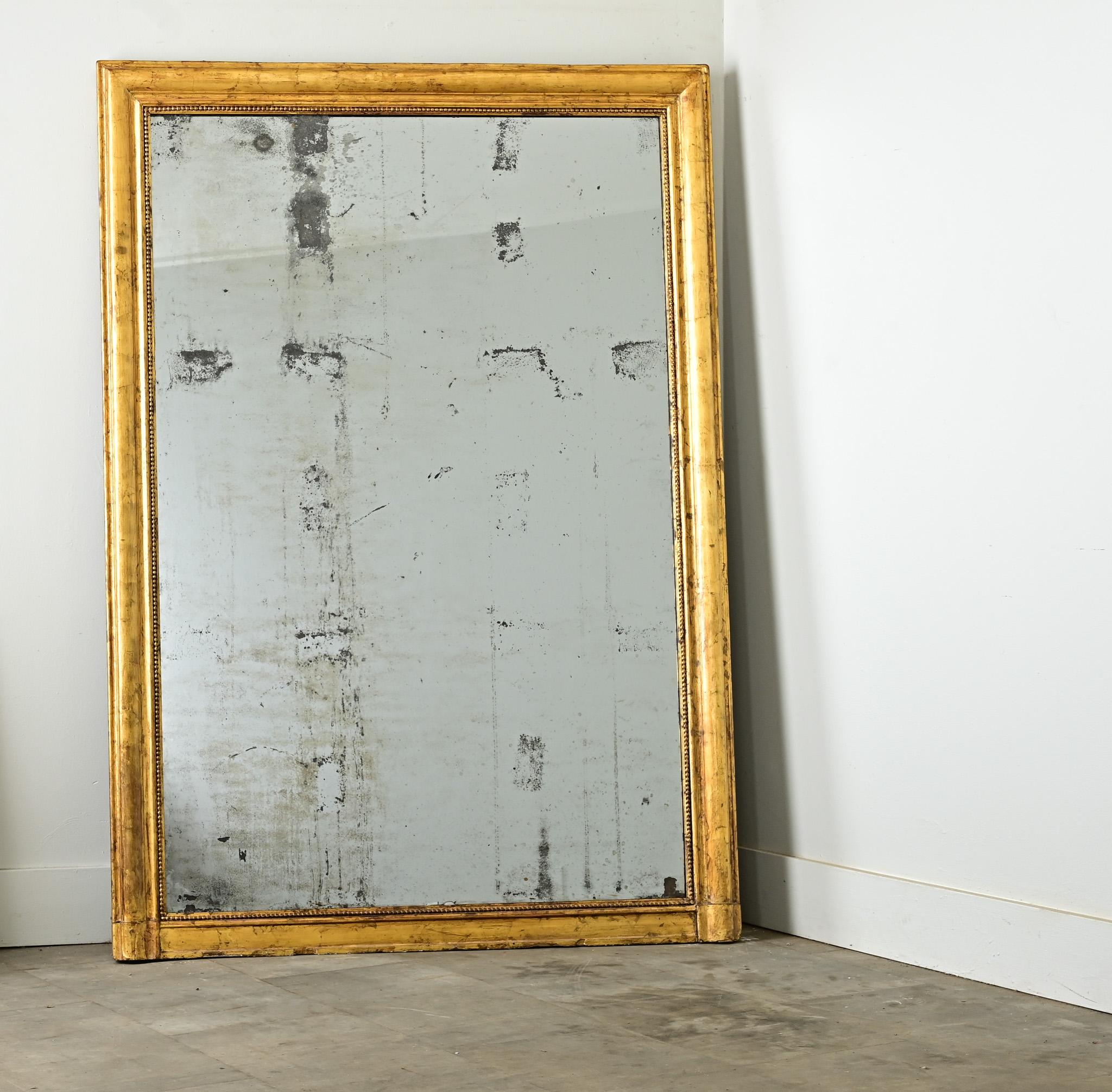 Abstract foxing of the original glass is what characterizes this French mantle mirror. The large mirror plate is framed by classic and unassuming carved molding of textured gold gilt. Reflecting a mature patina, the frame is streaked with oxidation