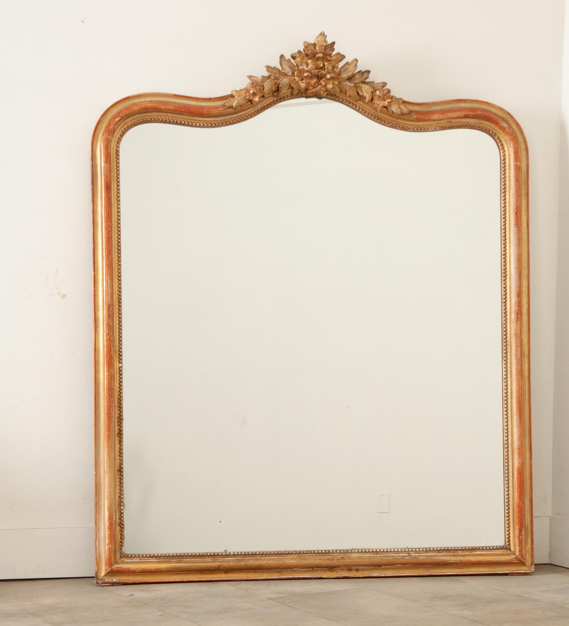 A gorgeous large scale gilt carved wood wall or mantel mirror crafted in 19th century France. The original mercury mirror is in great condition and its shaped frame is surrounded by a handsome carved bead border. This mirror has a lovely centered
