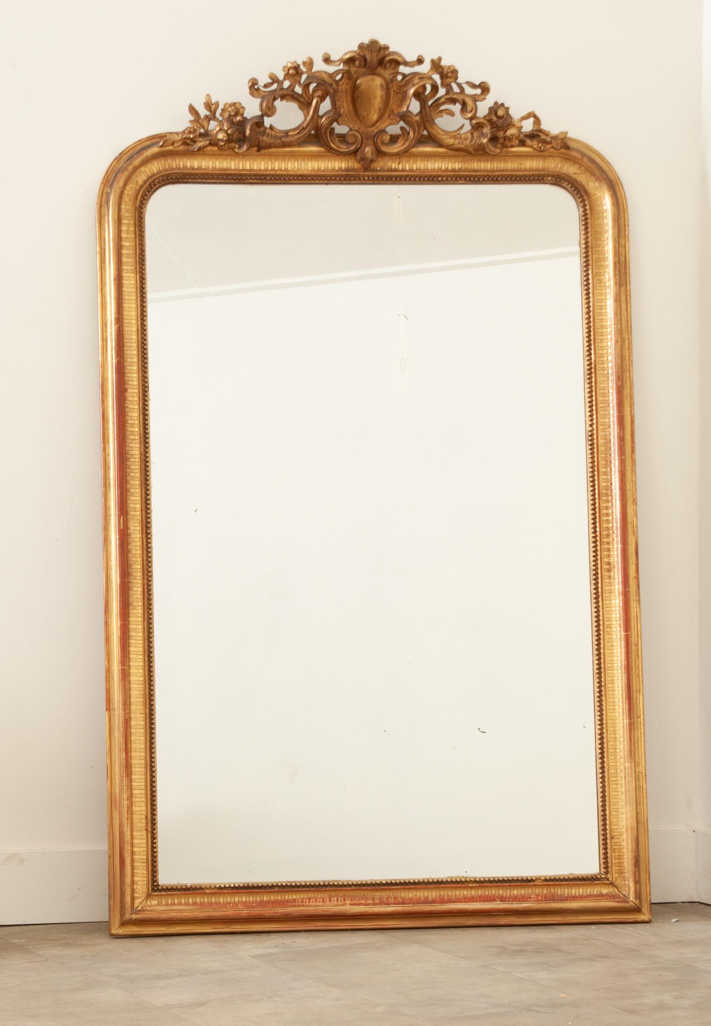 A striking Louis XVI style gold gilt mirror hand-crafted in France in the 19th century. This elegant mirror boasts the original mirror glass, still beautiful and showing signs of foxing and a few marks. The hand-carved frame is topped with an ornate