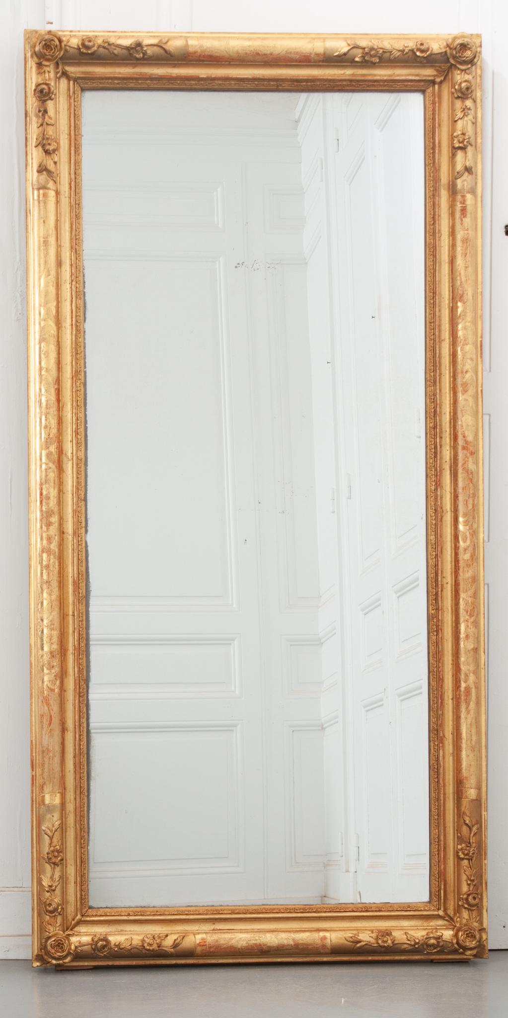 This 19th century French mirror is full of lovely floral details! The rectangular gilt frame is ornamented with floral etching on all sides and low relief carvings in each corner. Worn over the years, the red base paint peaks through the gold gilt,