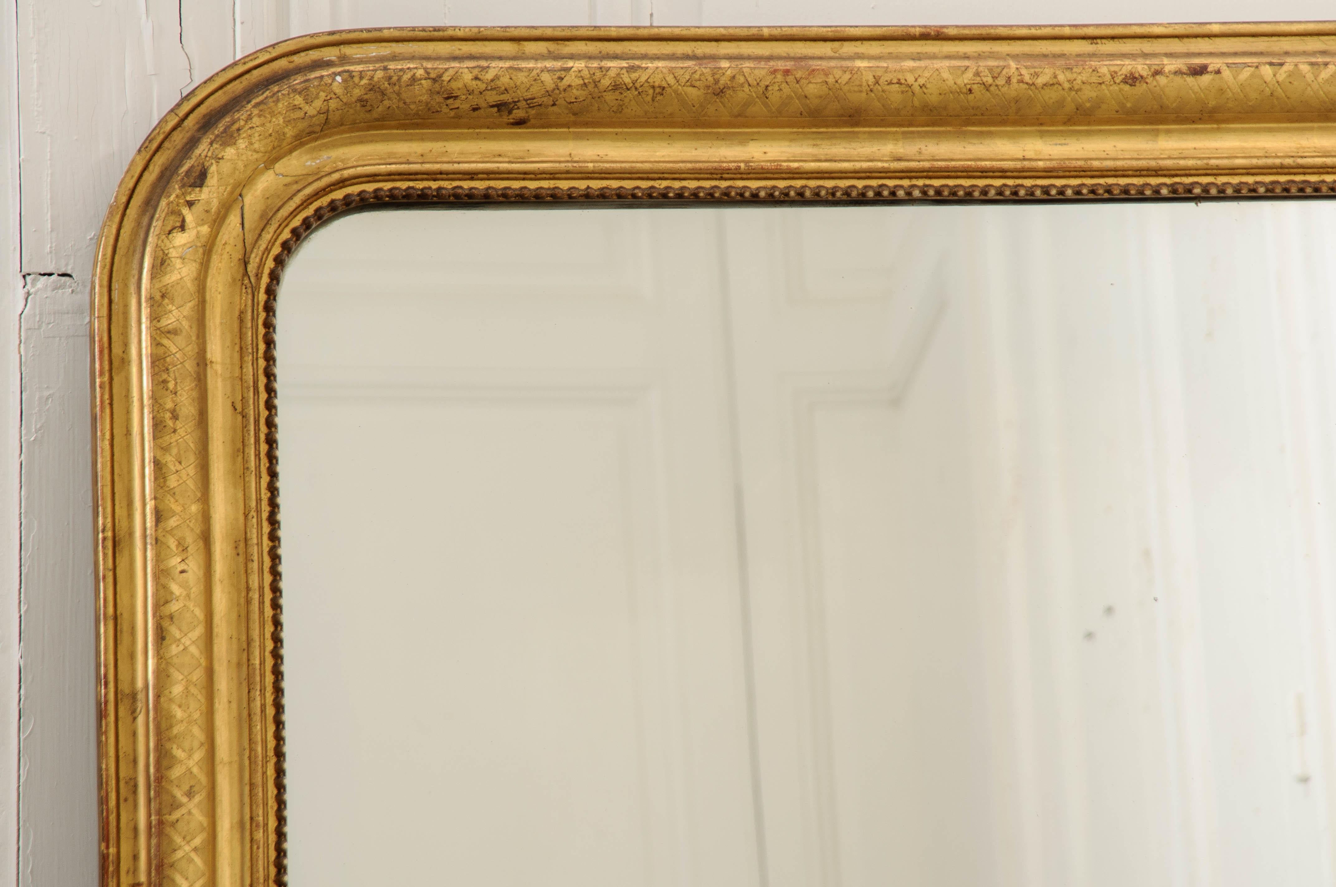 A fabulous gold gilt Louis Philippe mirror, with its iconic shaped frame. This 19th century French antique piece has remarkably intact gold gilt that is brilliant and lustrous. It has been finished with an etched cross-hatch design that provides
