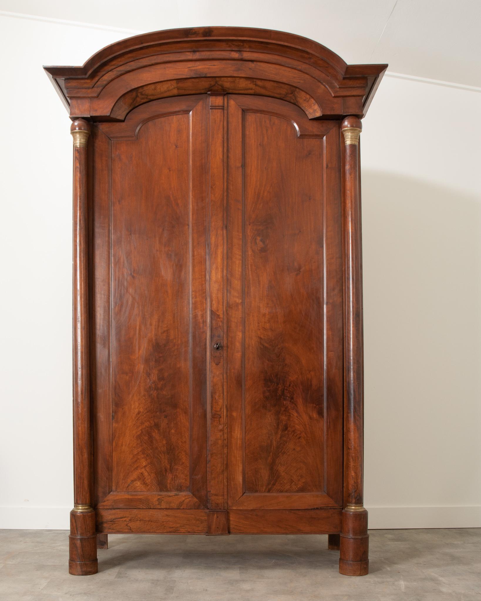 This massive Empire style armoire was crafted in 19th century France from stunning walnut. At over 8.5 feet tall, this massive armoire is crowned with a Chapeau de la Champ style bonnet – named after the hats worn by French military field officers