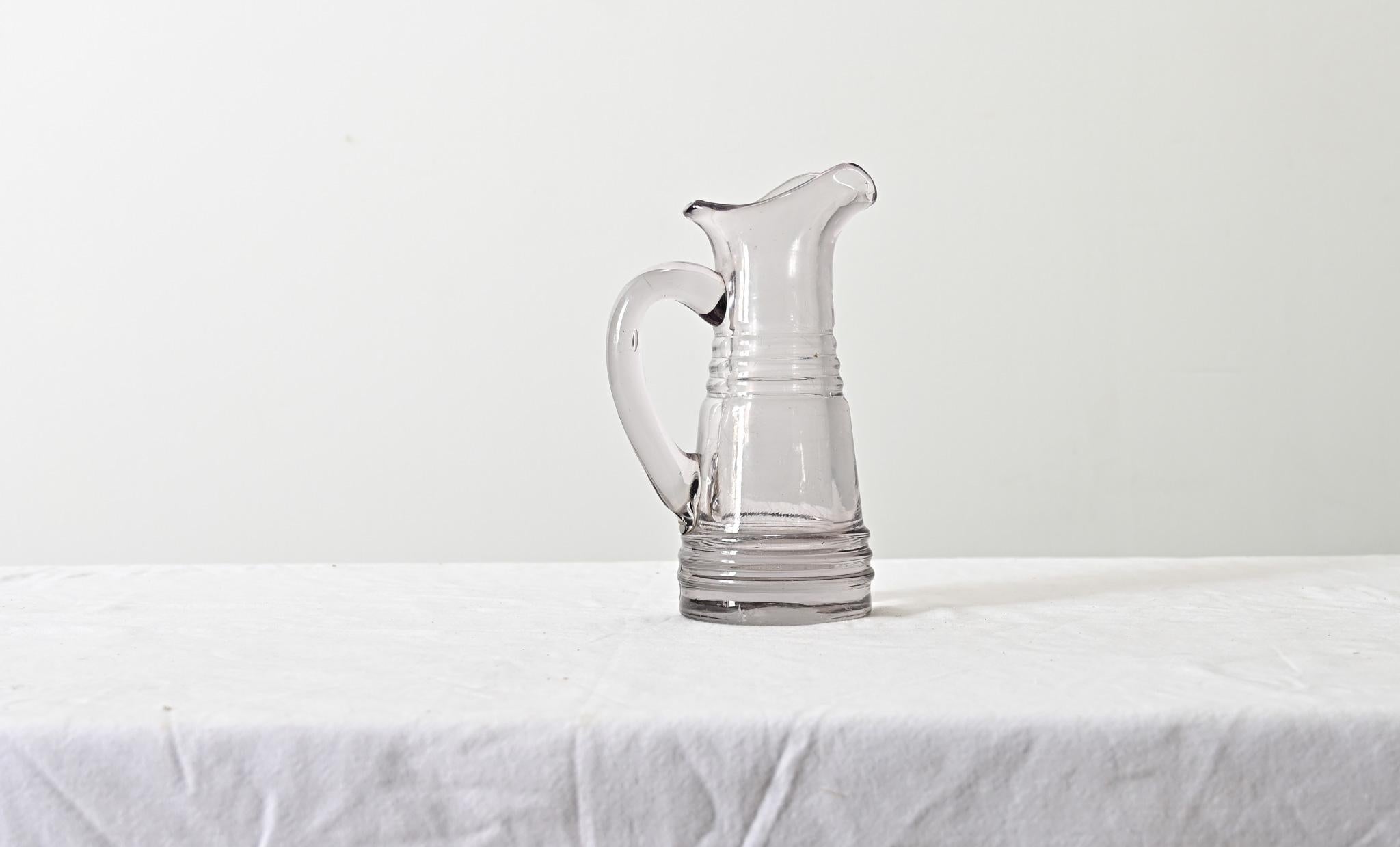 French, 19th century handmade glass pitcher from the Normandy region, likely used for cider as Calvados (the apple brandy) is made in the same region. The heavy glass vessel uses an elegant spout for pouring, balanced by a solid handle with gorgeous