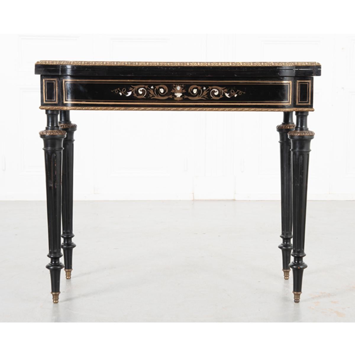 Cette magnifique table de jeu ébonisée datant du 19ème siècle en France attirera tous les regards dans n'importe quel espace ! Dans son état plié en console, une urne complexe et un cimier floral avec incrustation de laiton et de nacre ornent le