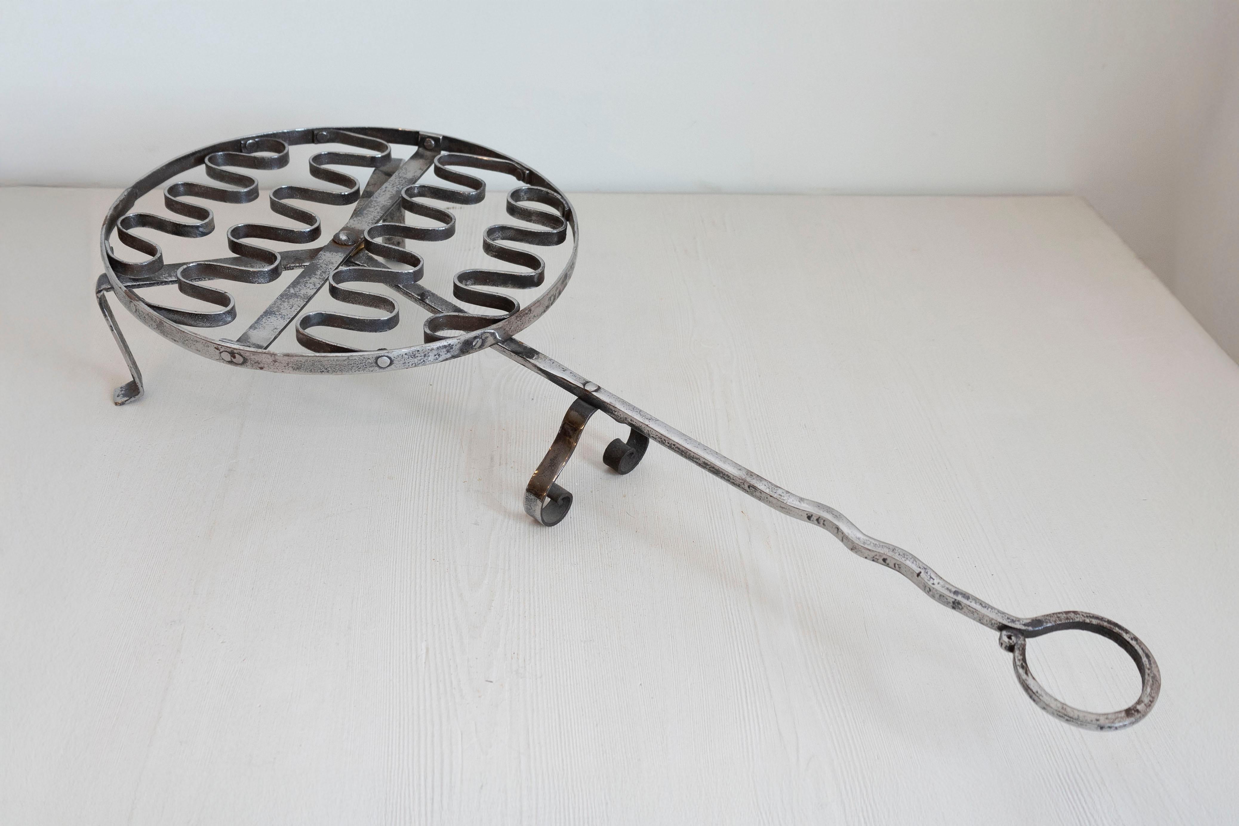 A French iron grill from the 19th century, with petite feet and long handle. Created in France during the 19th century, this iron grill was used as a tool in a fireplace. Featuring a circular body resting on petite feet, the grill showcases a long