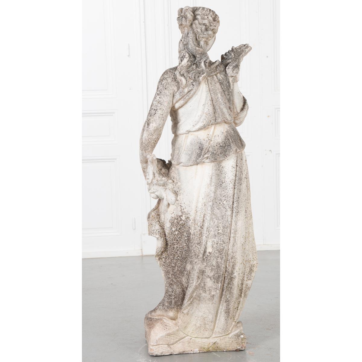 This patinated cast stone statue would work beautifully indoors or outdoors. It is French and from the 19th century. It depicts a robed female with one hand on her shoulder draping a garland of flowers across her body to her opposite hand. Peeking