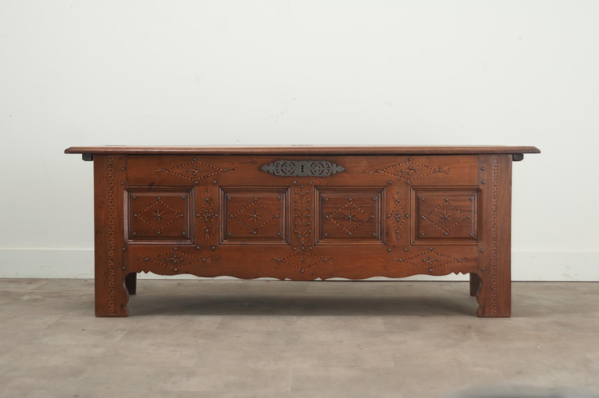 A large French solid oak paneled coffer. The front side has geometric inlay designs of ebonized wood, satinwood and hand forged nailheads over a playful scalloped apron. The hinged top opens to a large storage cavity with its classic candle box. A