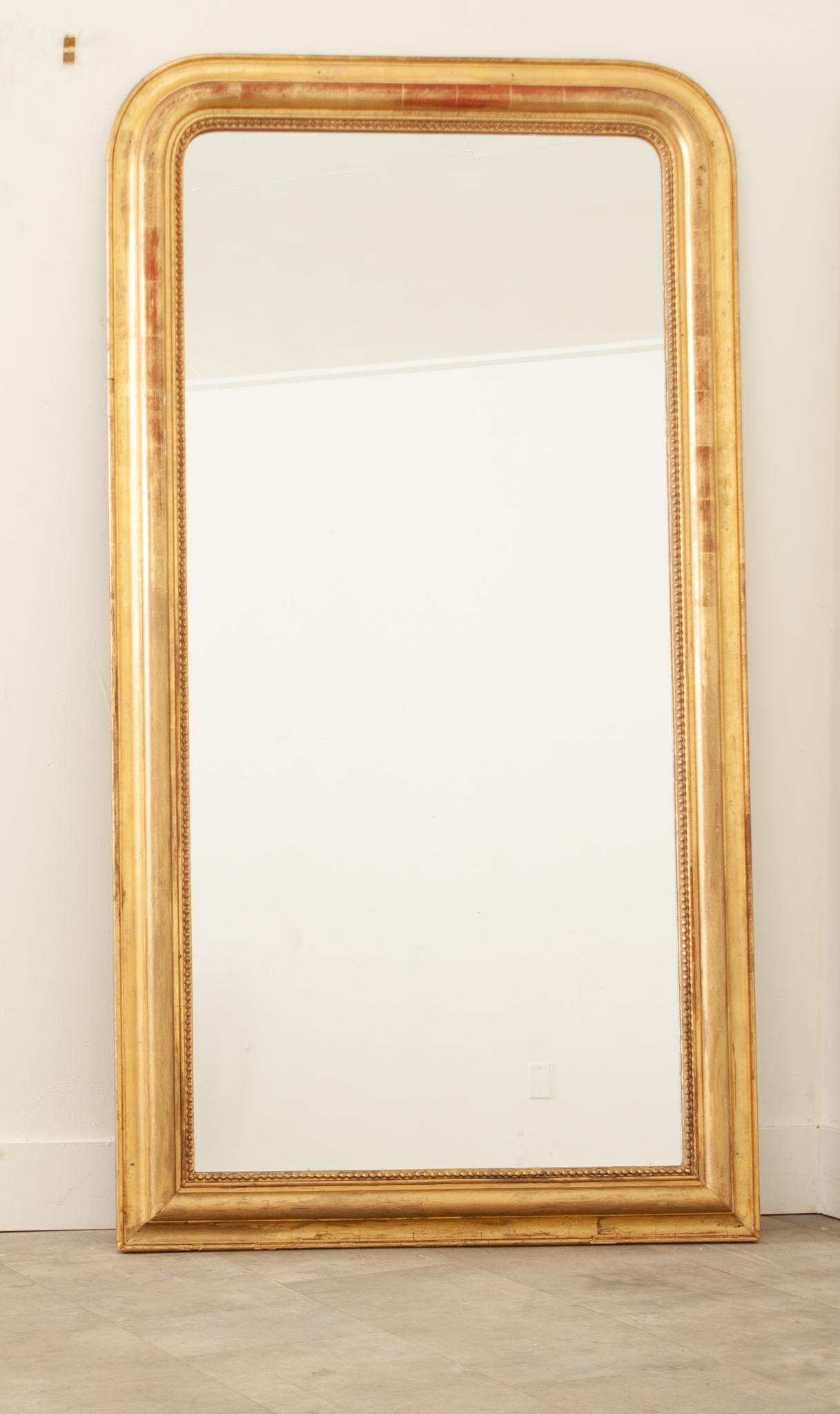 A large Louis Phillipe style floor mirror hand-crafted in France in the 19th century. This tall, elegant mirror with classic Louis Philippe style embellishments stands at over five feet with quite a commanding presence. The hand-carved frame has a