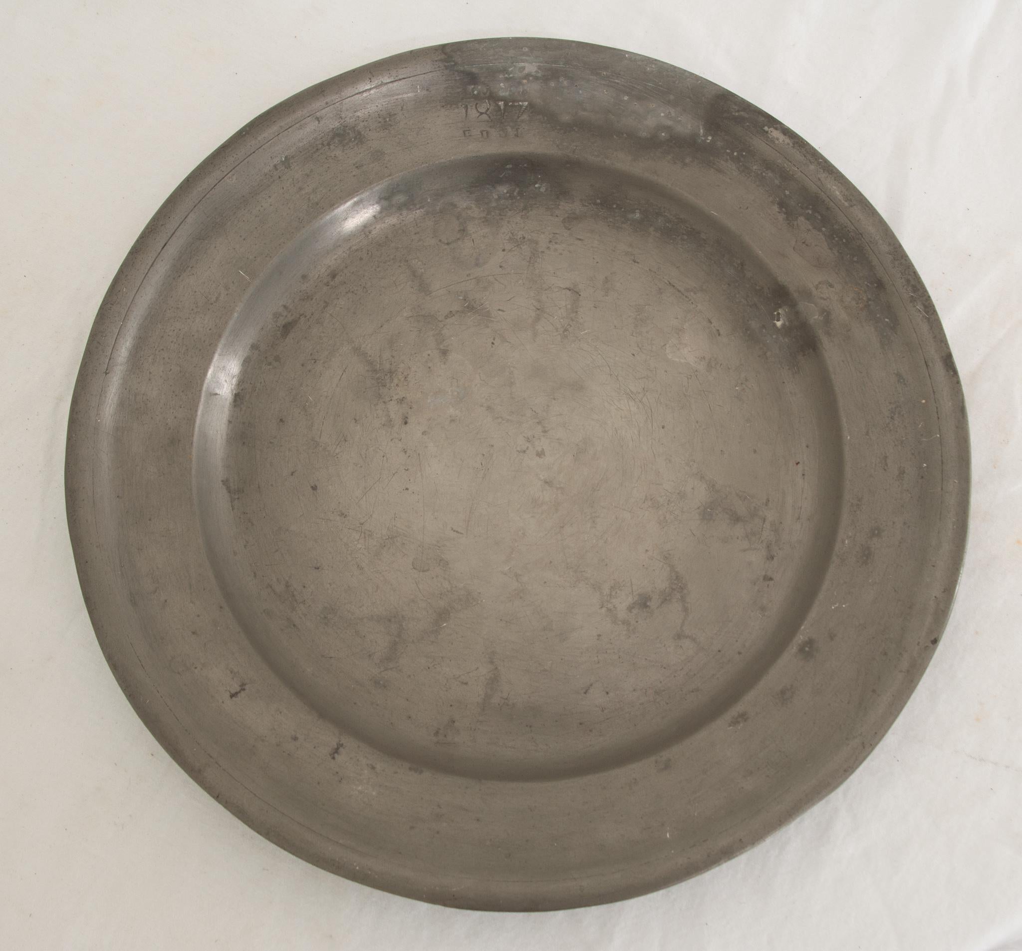 This large pewter plate from France is a wonderful culinary accessory dating from 1817. It has a fantastic patina and the perfect amount of wear. The date is etched into the top and the back showcases multiple stampings from the unknown pewterer.