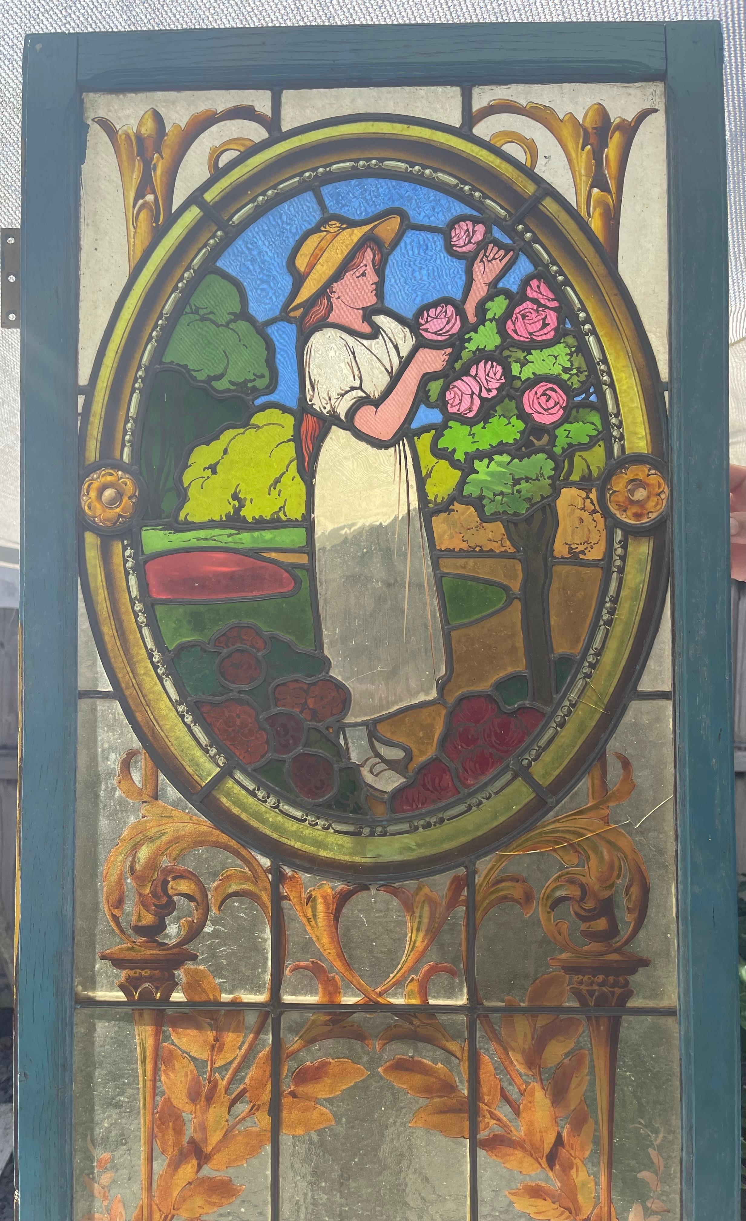 Beautiful old stained glass window from 1890 representing a countryside scene. At its base, a work of glass in the form of a shell reveals a vase and its acanthus leaves. On the top of the panel, a women picking up some roses , all made of different